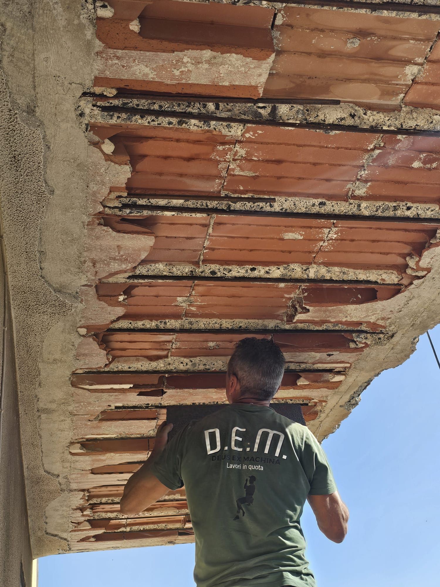 Uomo che esamina un soffitto in mattoni danneggiato con intonaco sgretolato. Indossa una camicia verde, all'aperto.
