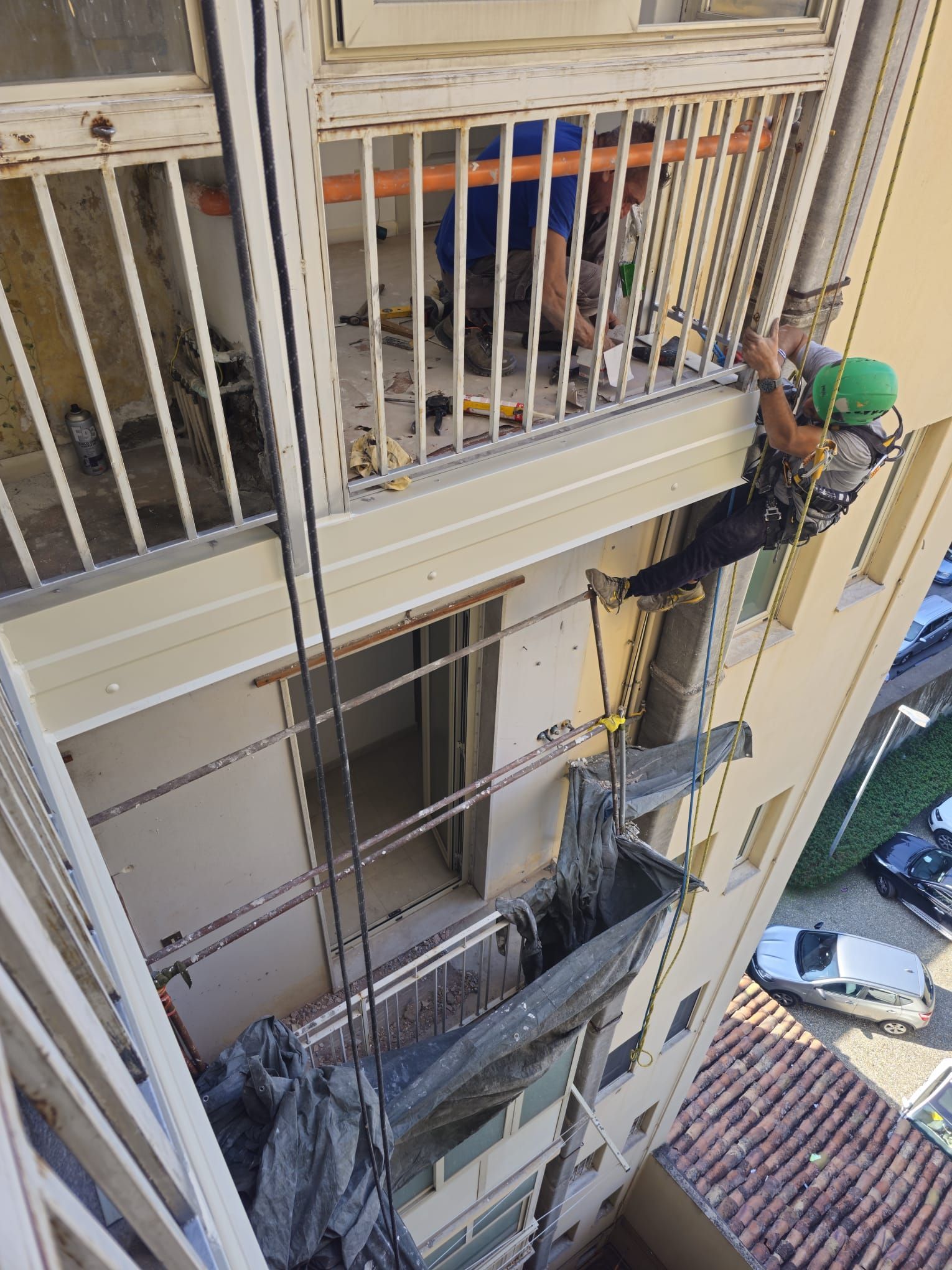 Operai edili su un grattacielo, uno dei quali è sospeso a una corda, mentre eseguono riparazioni esterne.