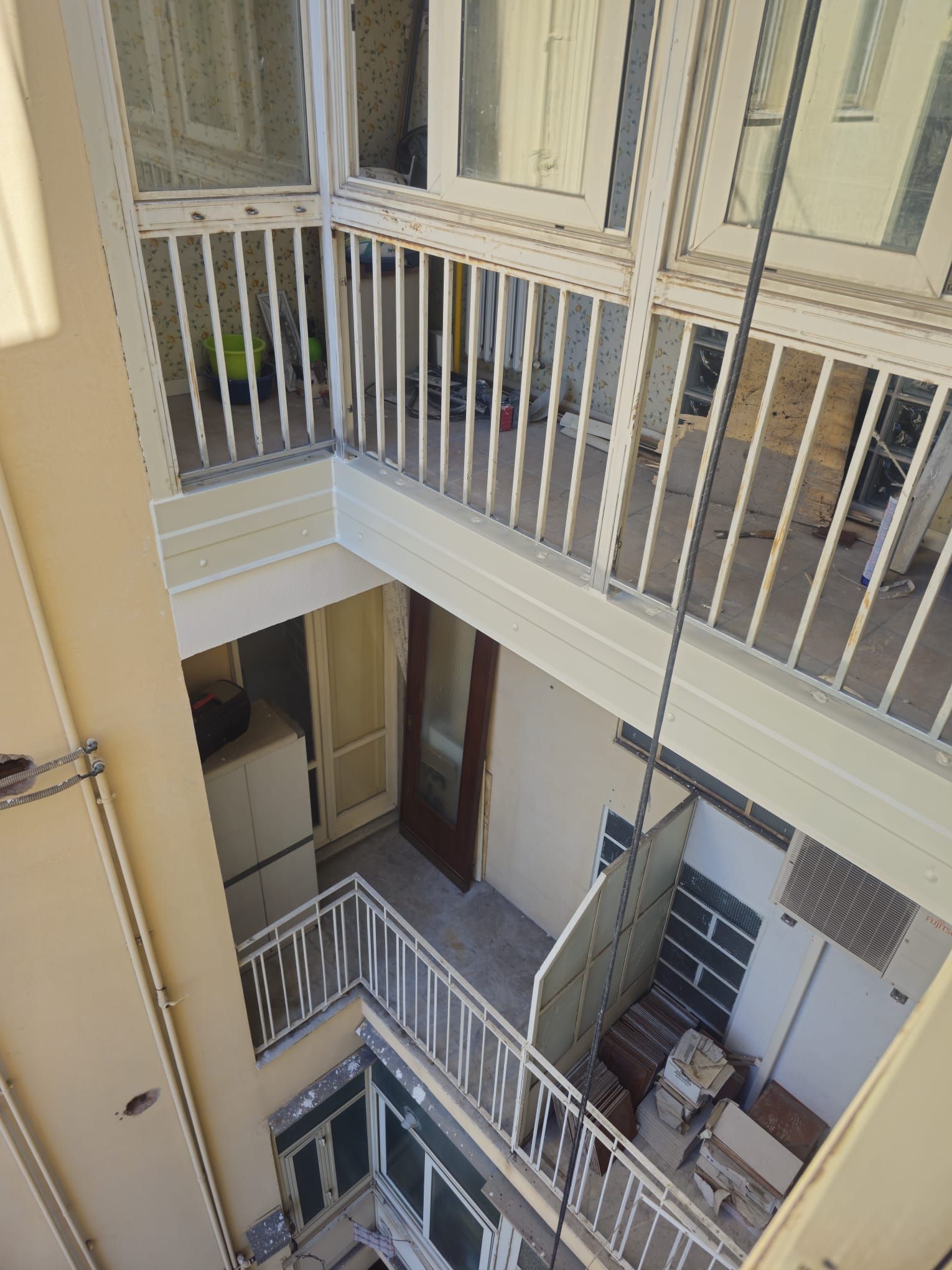 Vista dal balcone del cortile interno di un edificio a più piani con ringhiere, finestre e porte bianche.