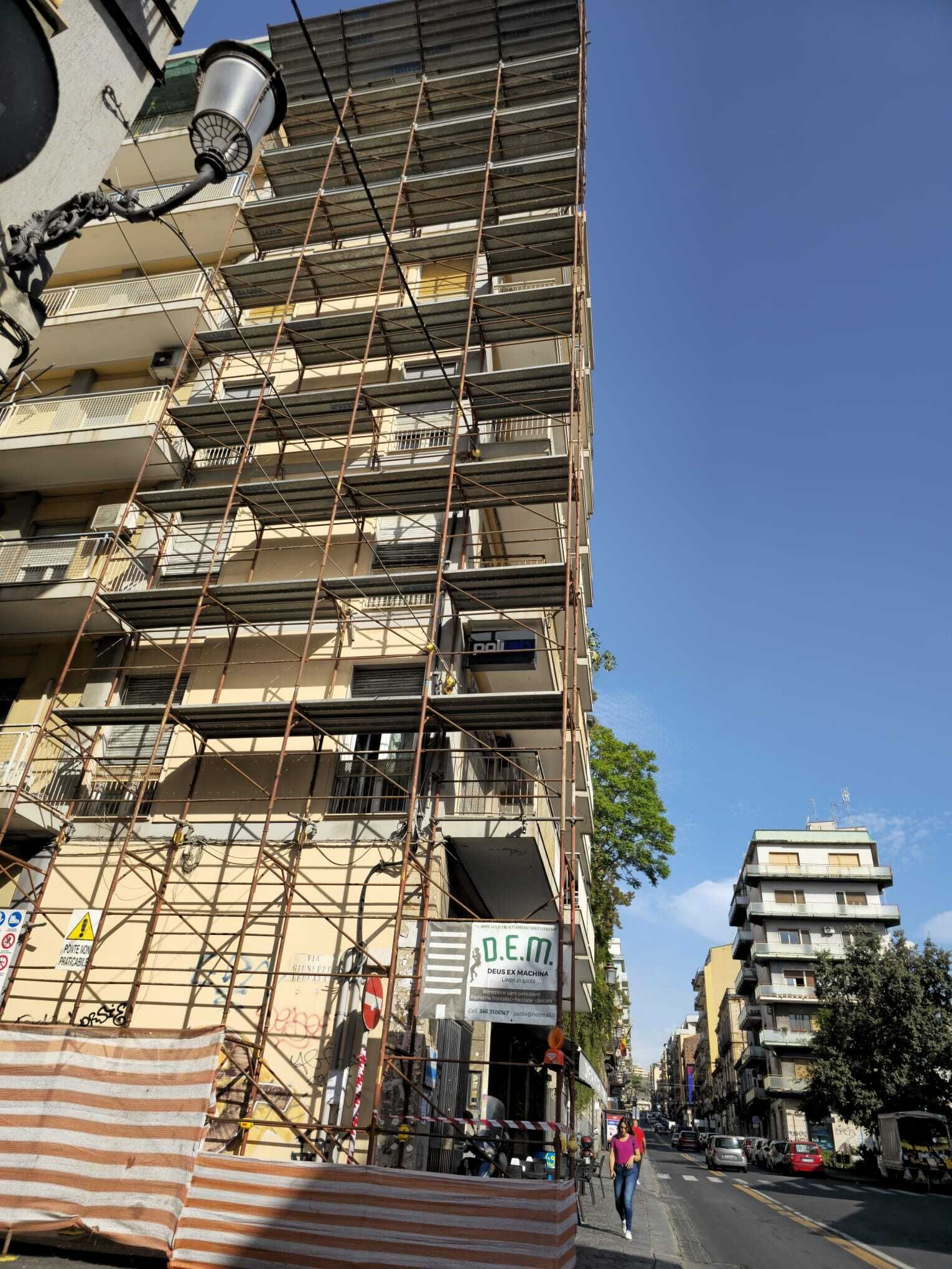 Edificio con impalcature, scena di strada. Edificio giallo in costruzione con un'attività commerciale al piano terra. Cielo azzurro.