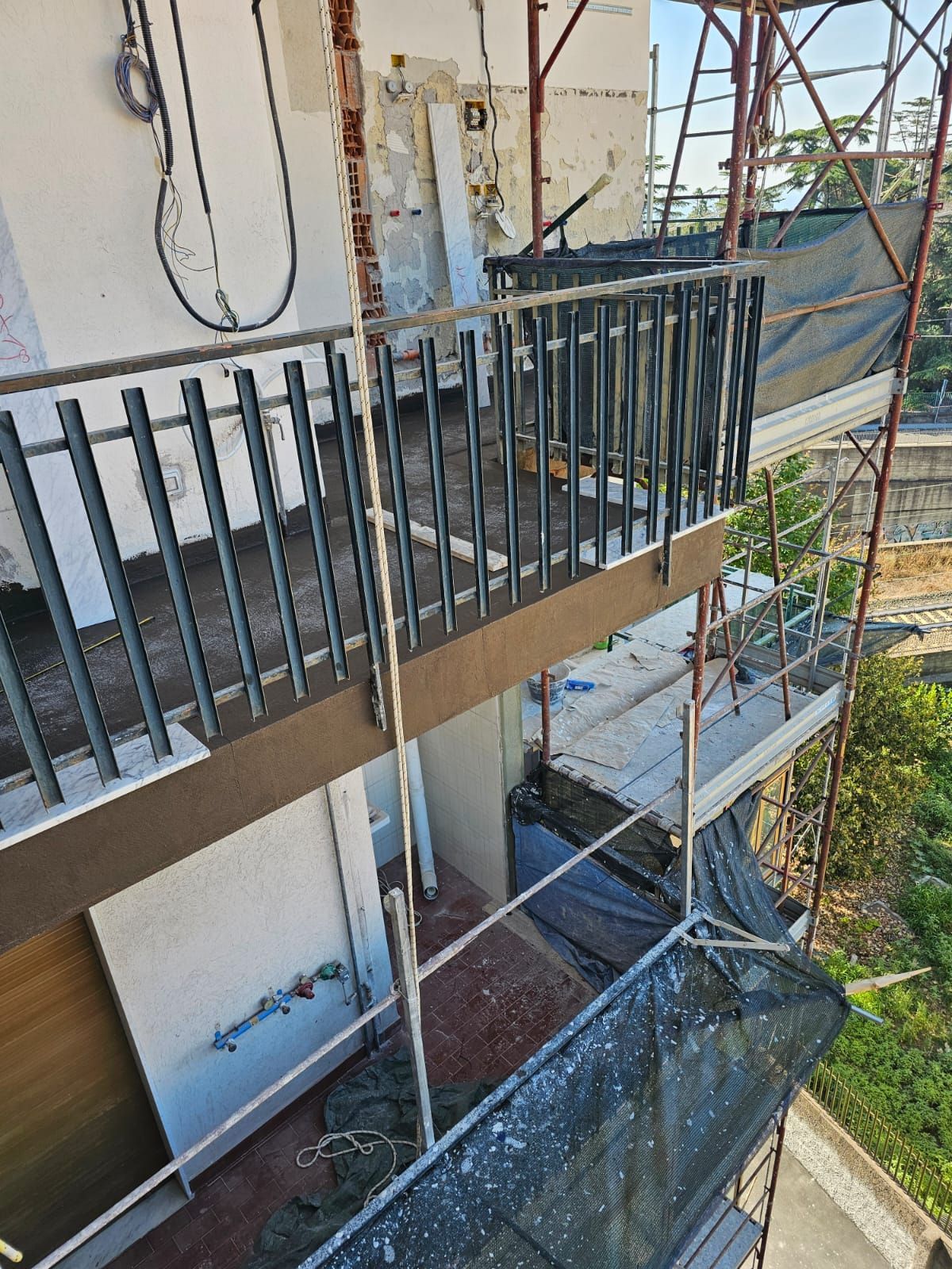 Persona che si cala in corda doppia dalla facciata di un edificio, tenendo in mano un secchio. Indossa dispositivi di sicurezza, mentre lavora su un edificio.