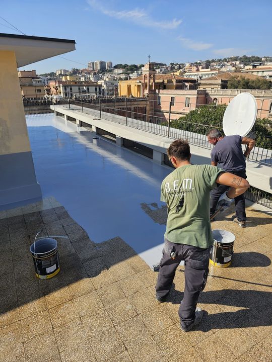 Due operai sigillano un tetto; sullo sfondo la città.