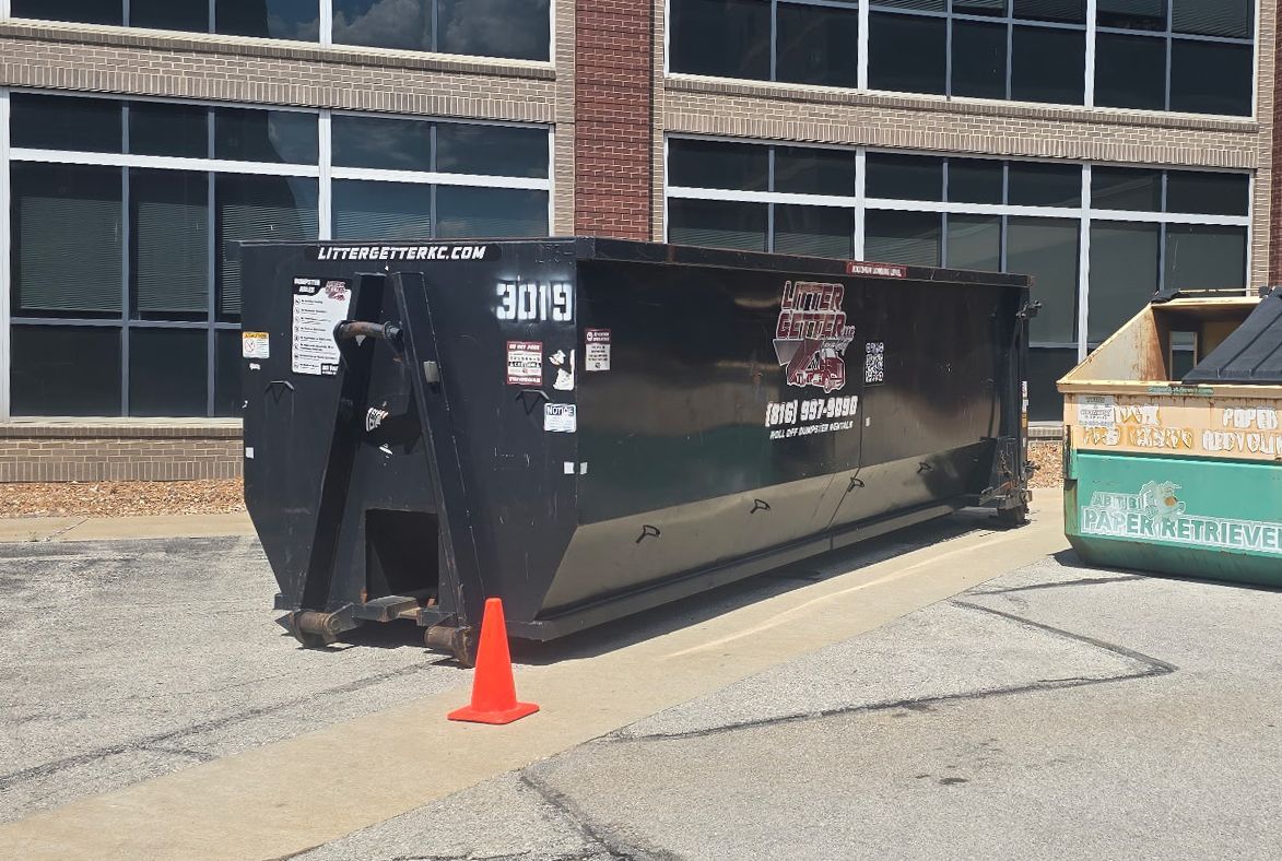 Black Litter Getter dumpster in Kansas City with a traffic cone in front of it, near a building with windows.