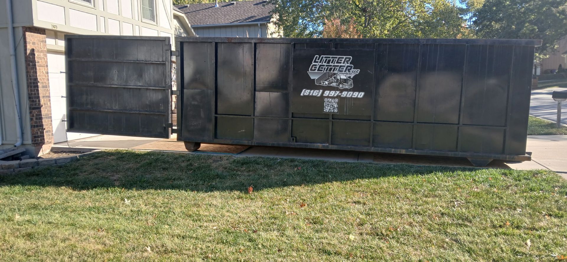 Black dumpster next to a building on a grassy lawn. The dumpster door is open.