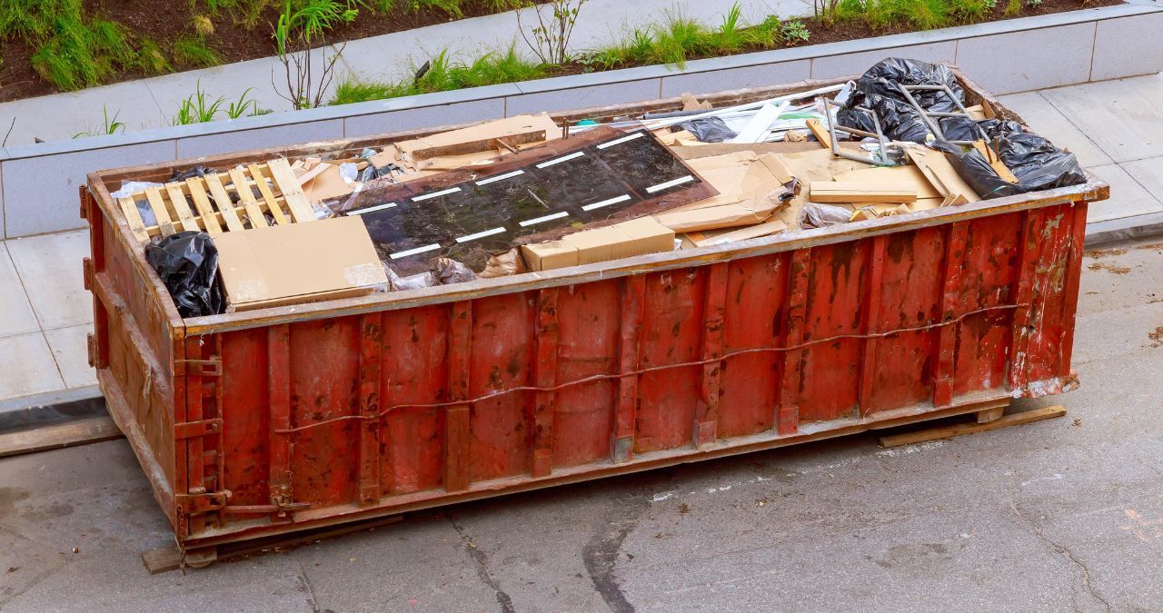 A large red dumpster filled with trash is sitting on the side of the road.