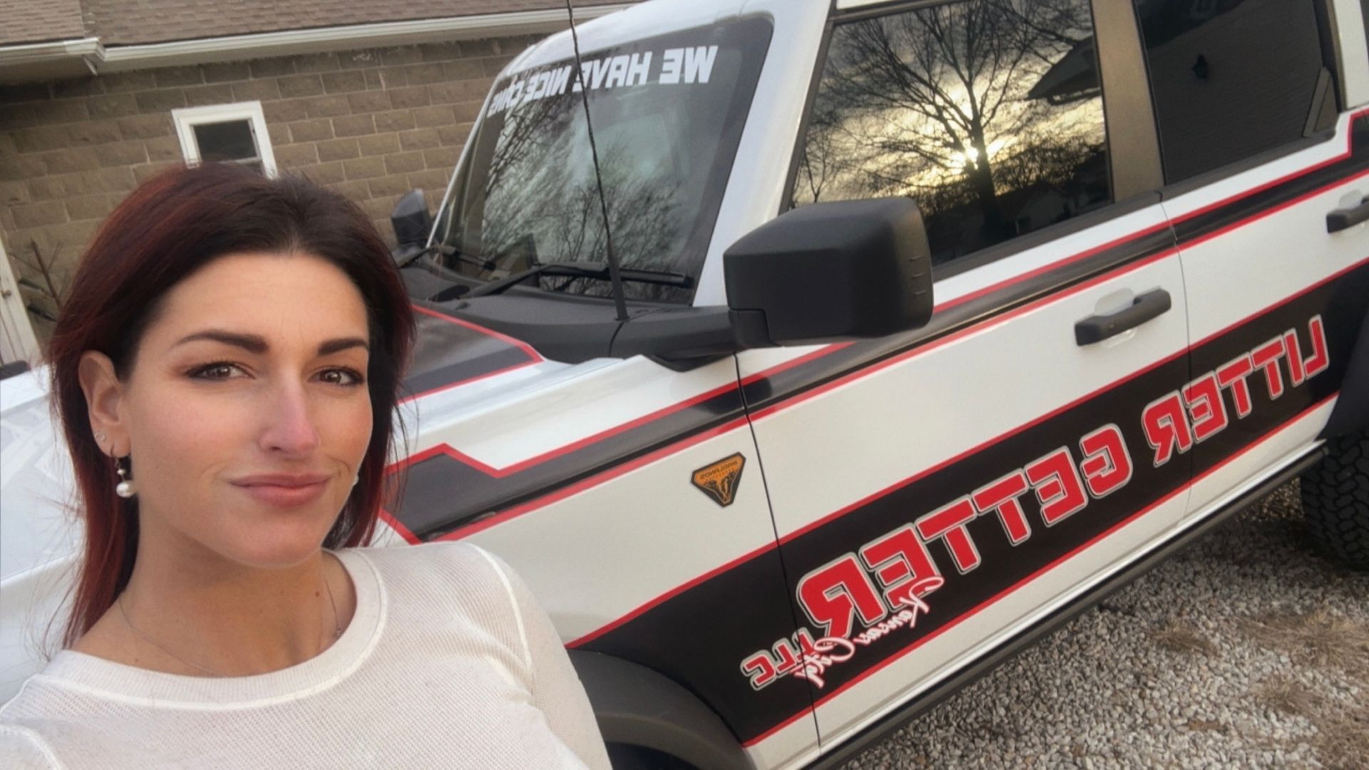 Woman in white top next to a white SUV with red and black graphics.