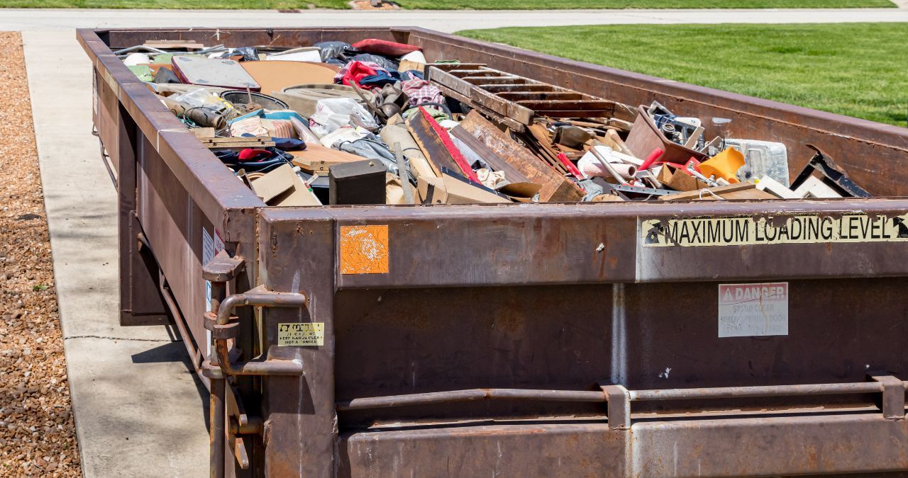 A dumpster filled with trash is parked on the side of the road.