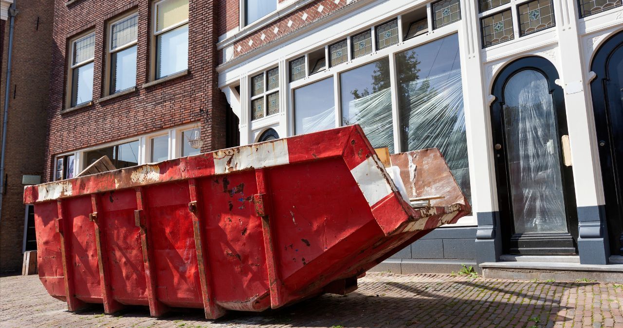 A red dumpster is parked in front of a building.