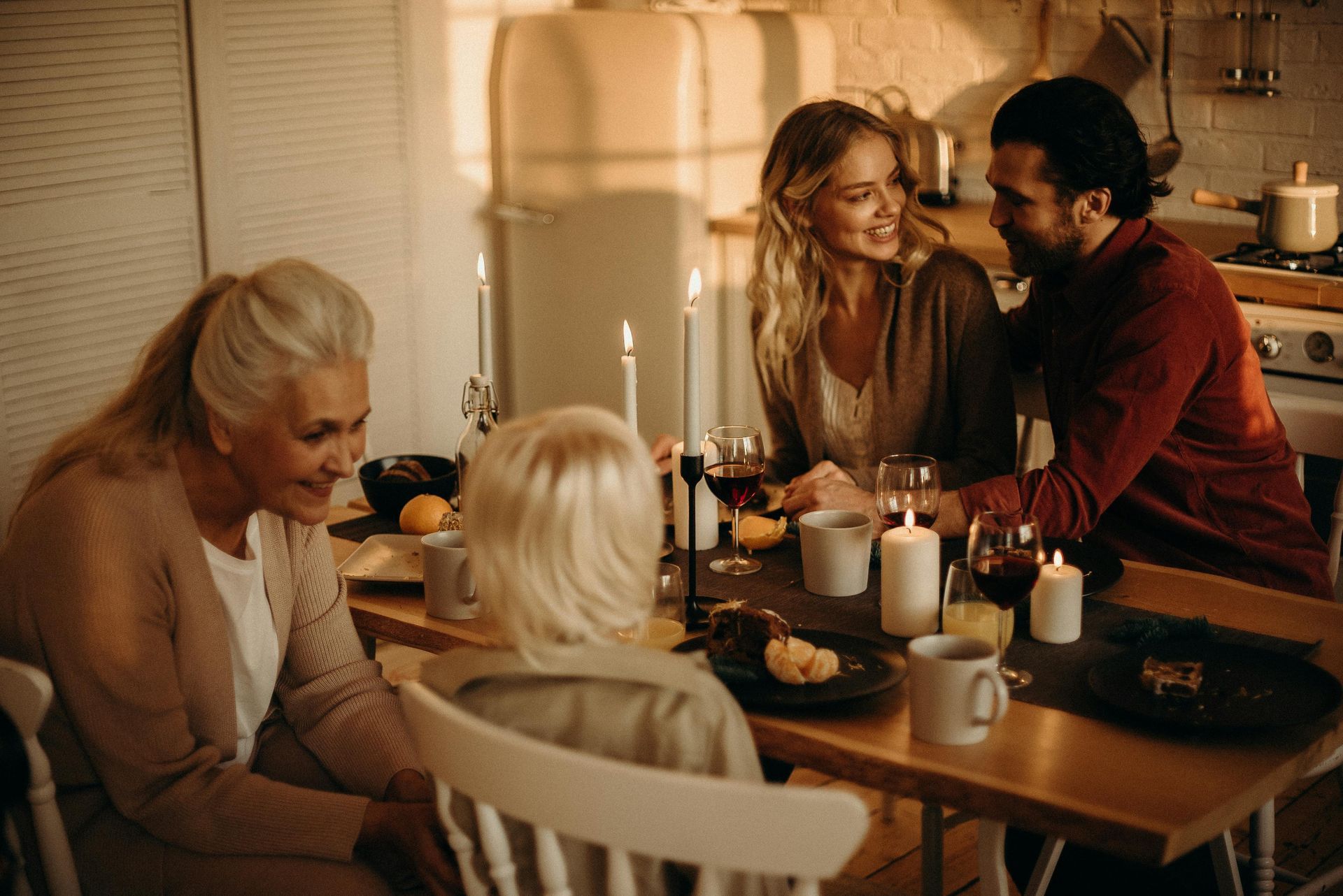 Family gathered at a dining table, lit by candles; smiling and talking in a warm kitchen.