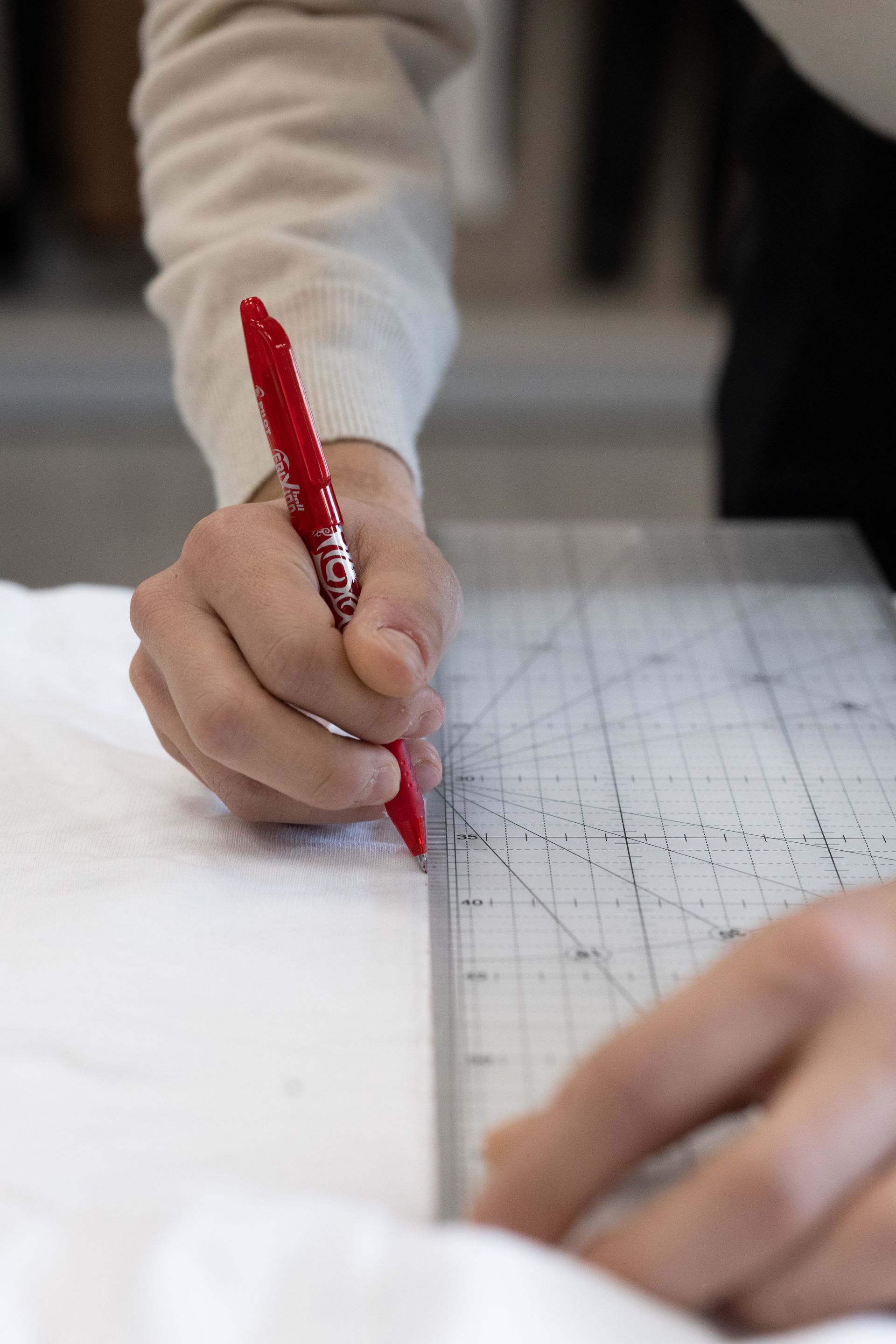 Persona che usa una penna rossa e un righello per tracciare una linea su un tessuto bianco.