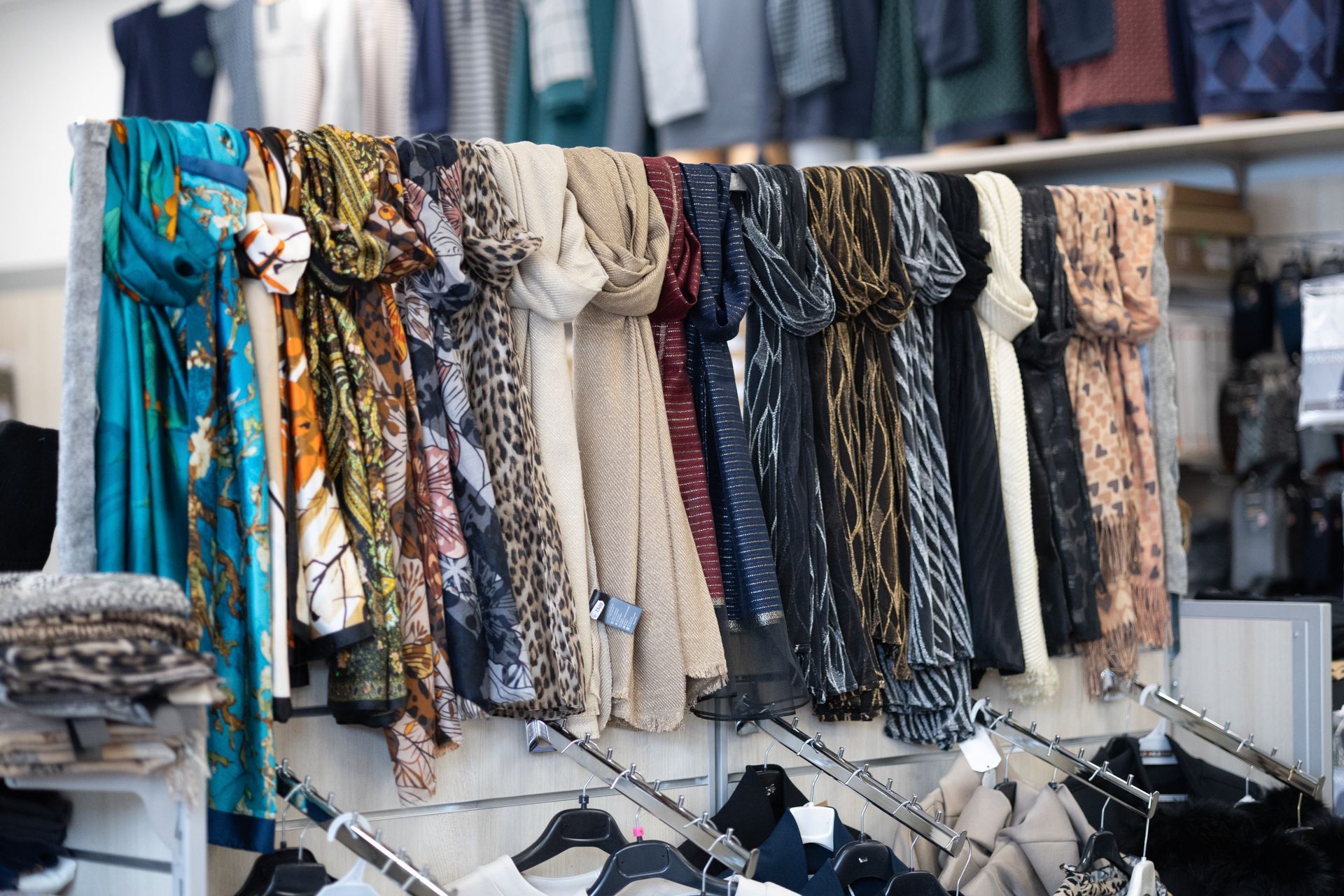 Sciarpe di vari colori e fantasie esposte su uno scaffale in un negozio.
