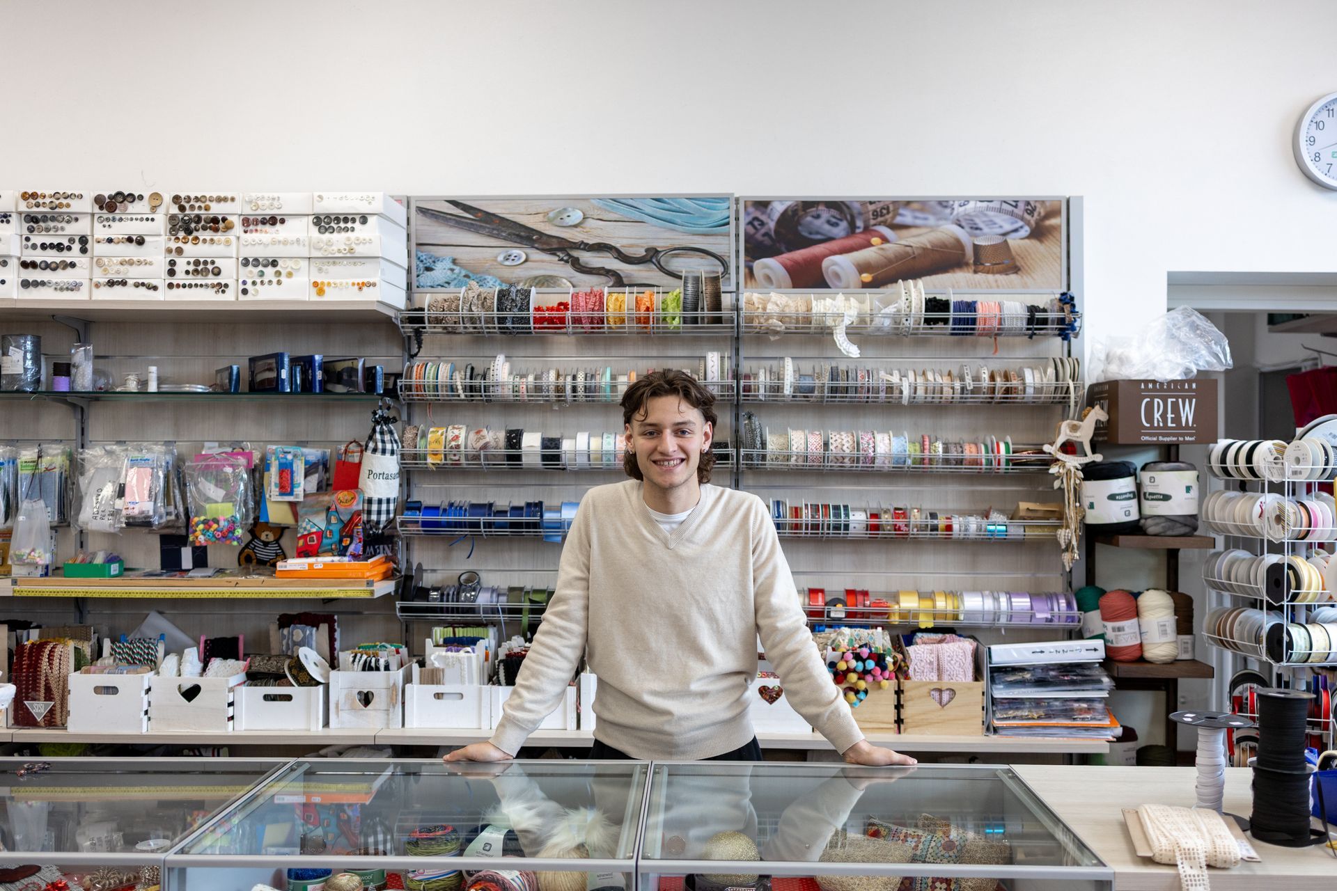 Una persona sorride dietro il bancone di un negozio di artigianato, rifornito di materiali.