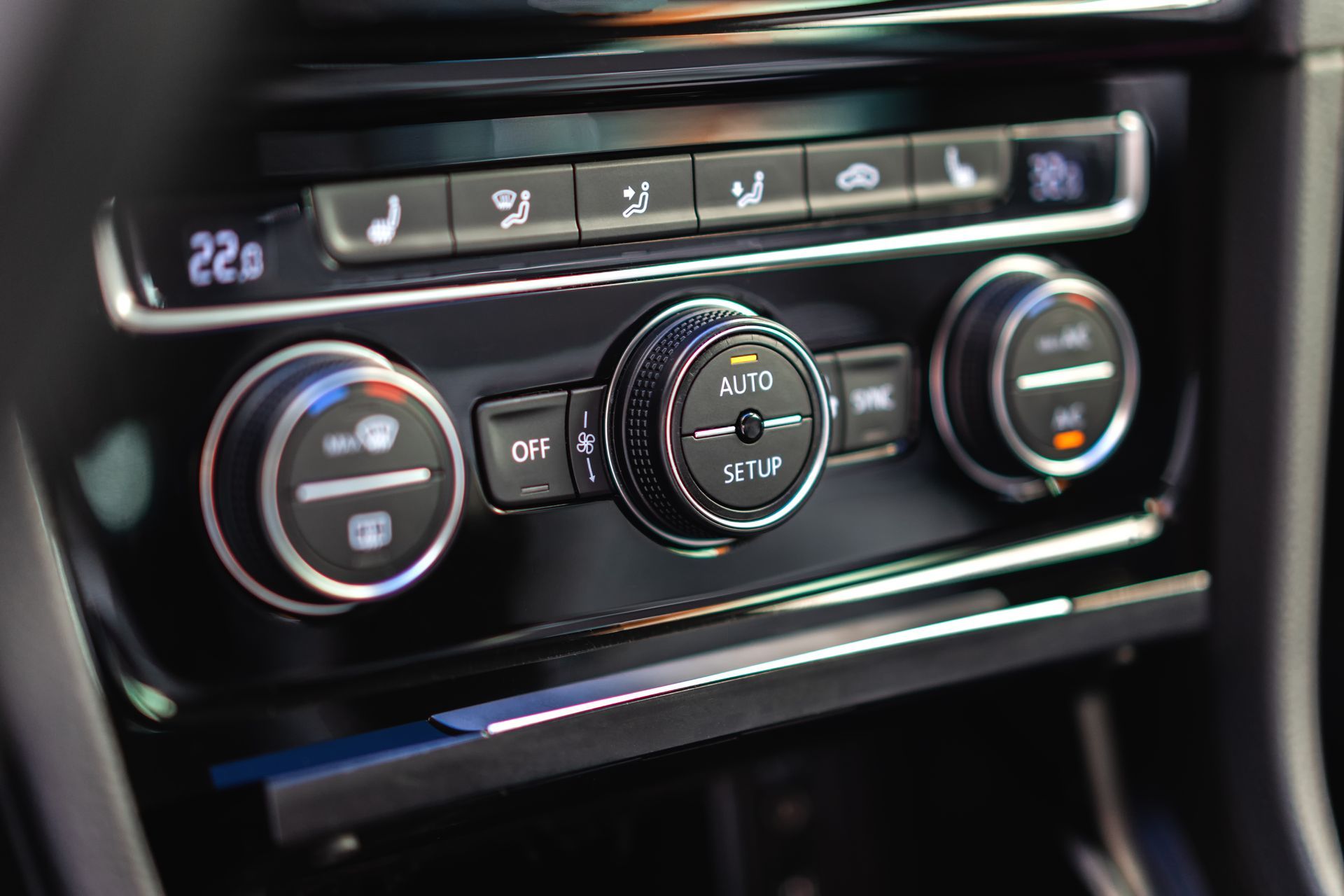 Car center console climate controls with illuminated temperature and fan dials in a black dashboard