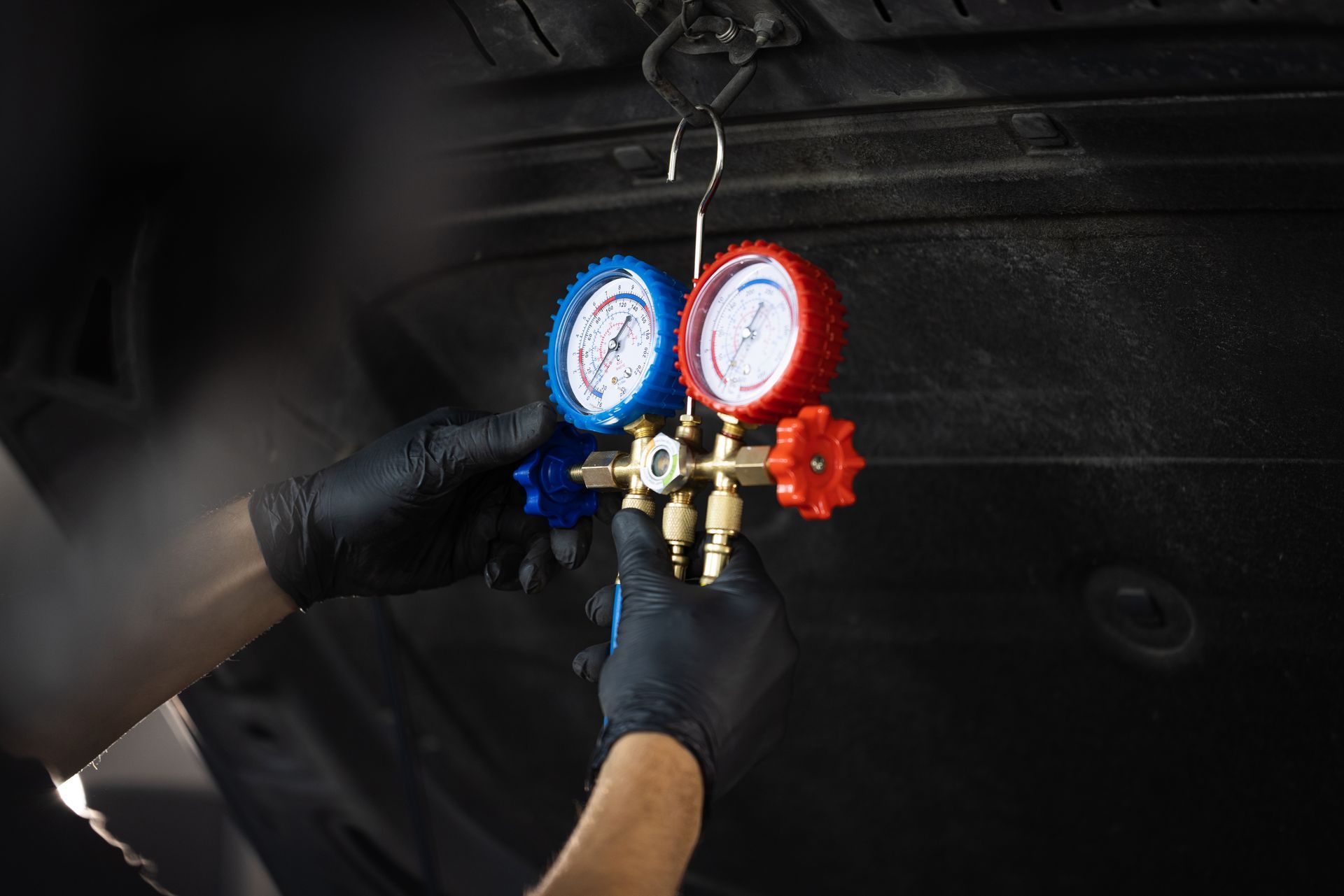 Gloved hands attaching blue and red gauges to an HVAC service valve on a dark unit