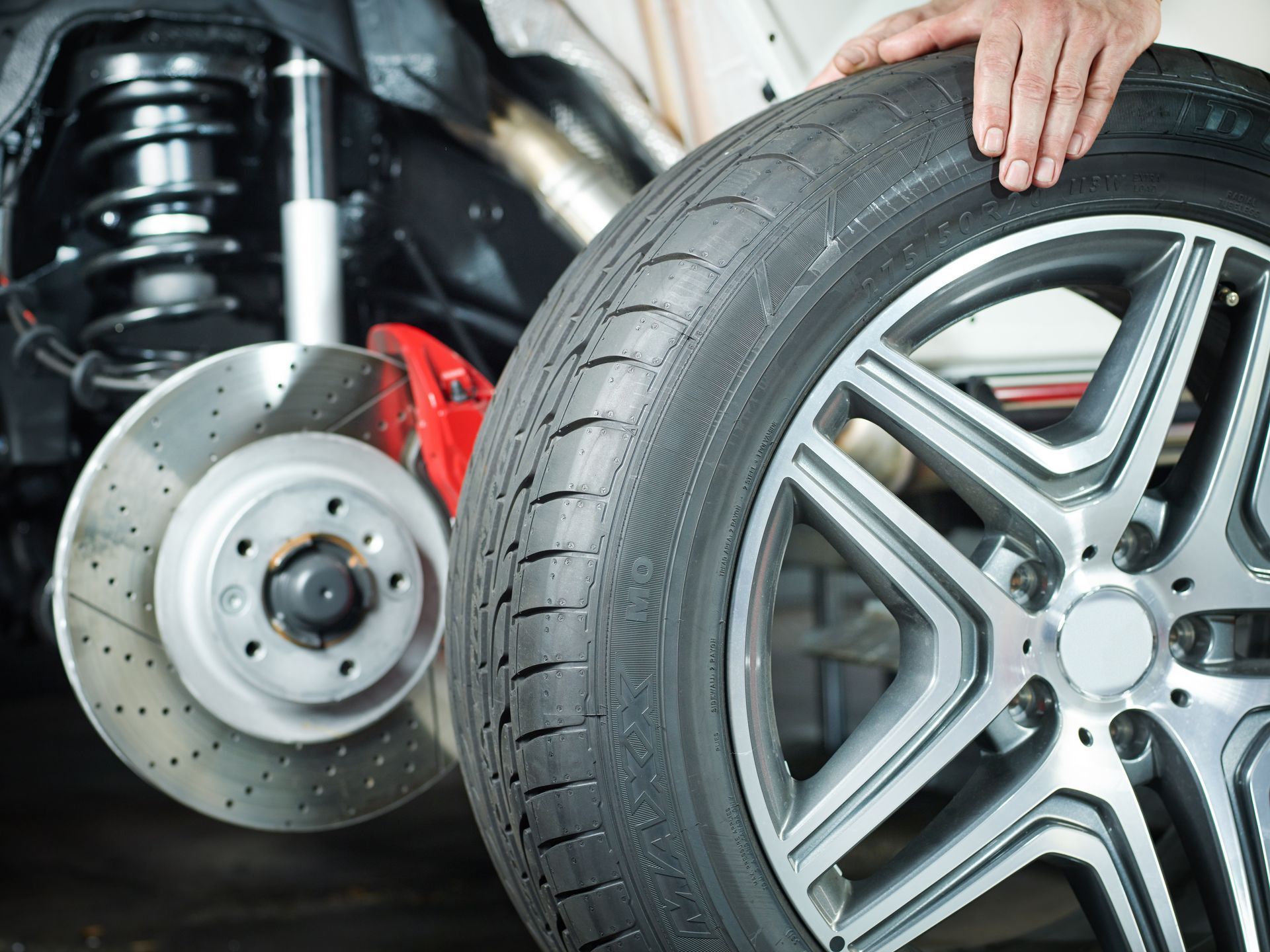 Car tire being held up beside a brake rotor and suspension in a car repair shop