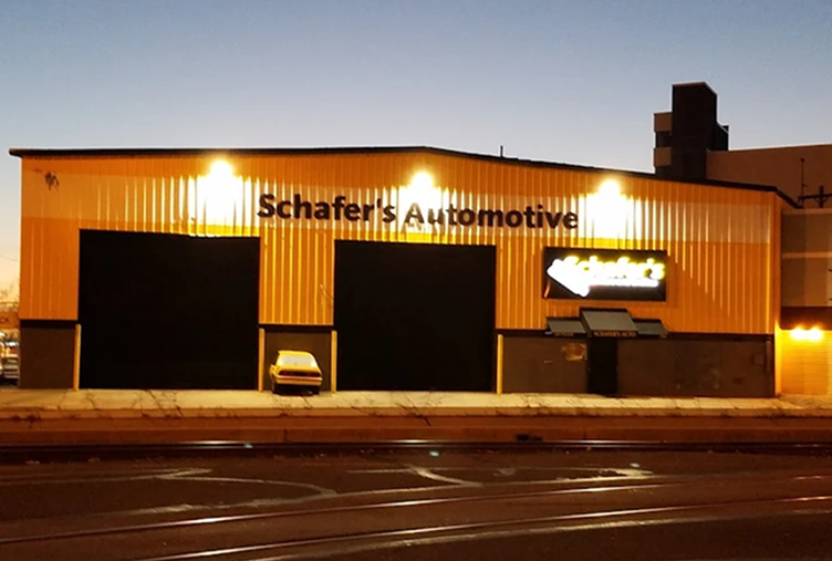 Schafter's Automotive storefront with open garage bays and a parked black car outside at dusk