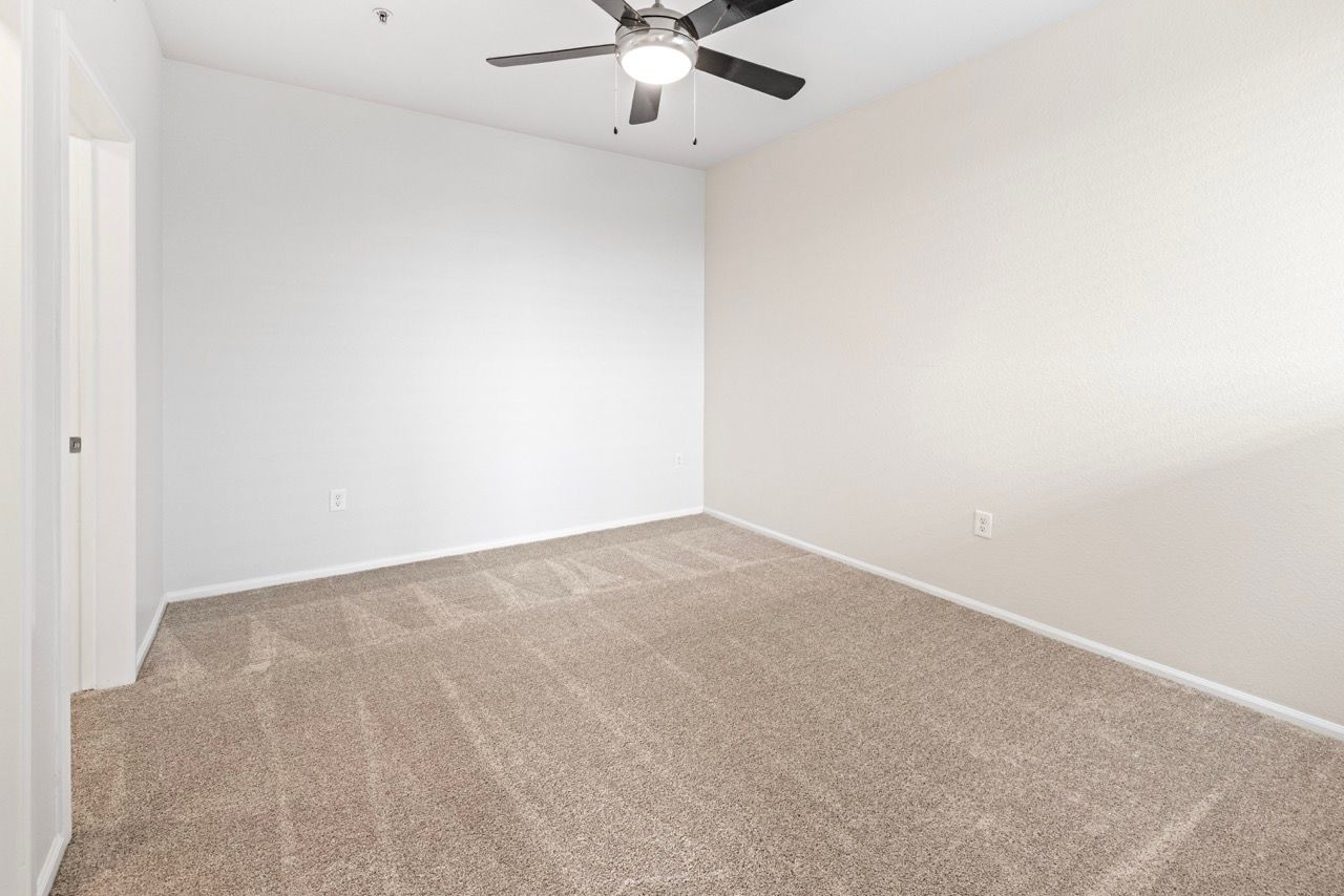 Empty bedroom with beige walls, carpet, and a ceiling fan.