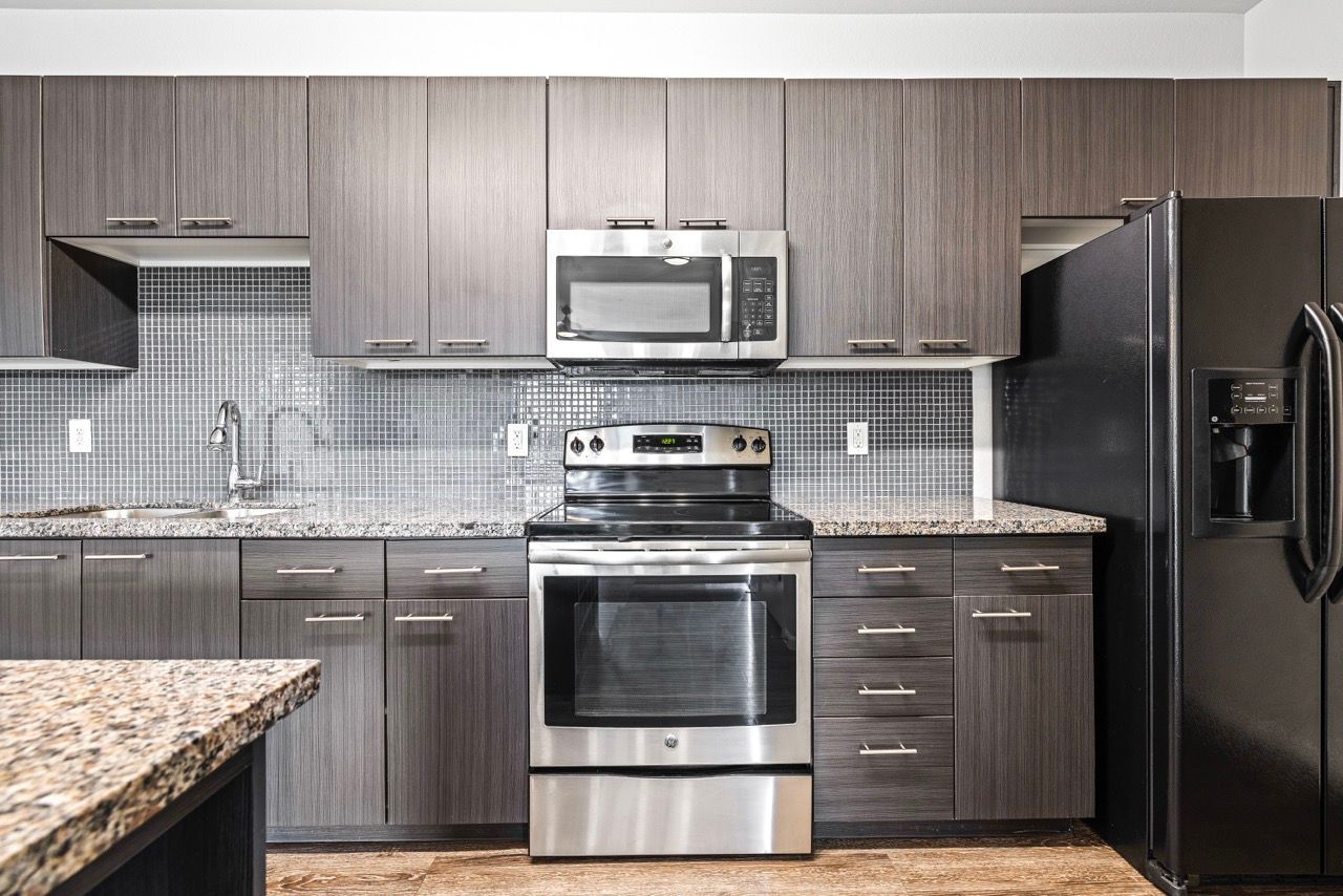 Modern apartment kitchen with dark wood cabinets, stainless steel stove and fridge, granite countertops.