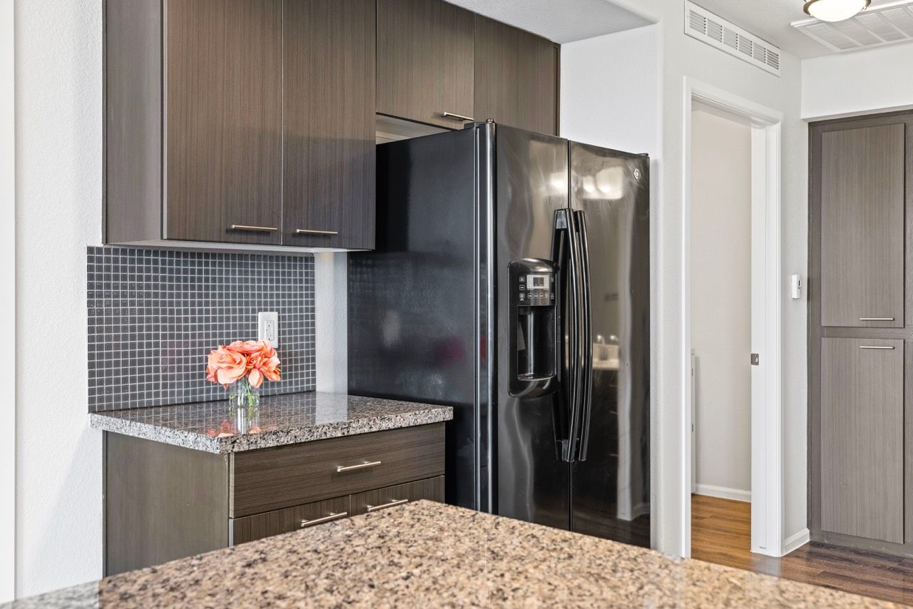 Modern kitchen with dark wood cabinets, granite countertops, a stainless steel side-by-side refrigerator, and a tiled backsplash.