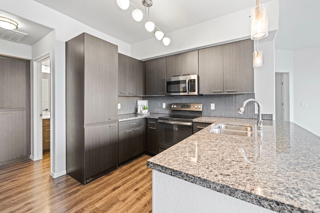 Modern kitchen with dark wood cabinets, granite countertops, island, and stainless steel appliances.