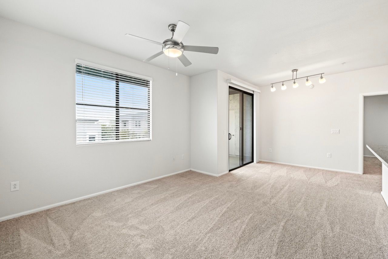 Bright living area with window blinds, a ceiling fan, and a sliding glass door to a balcony.