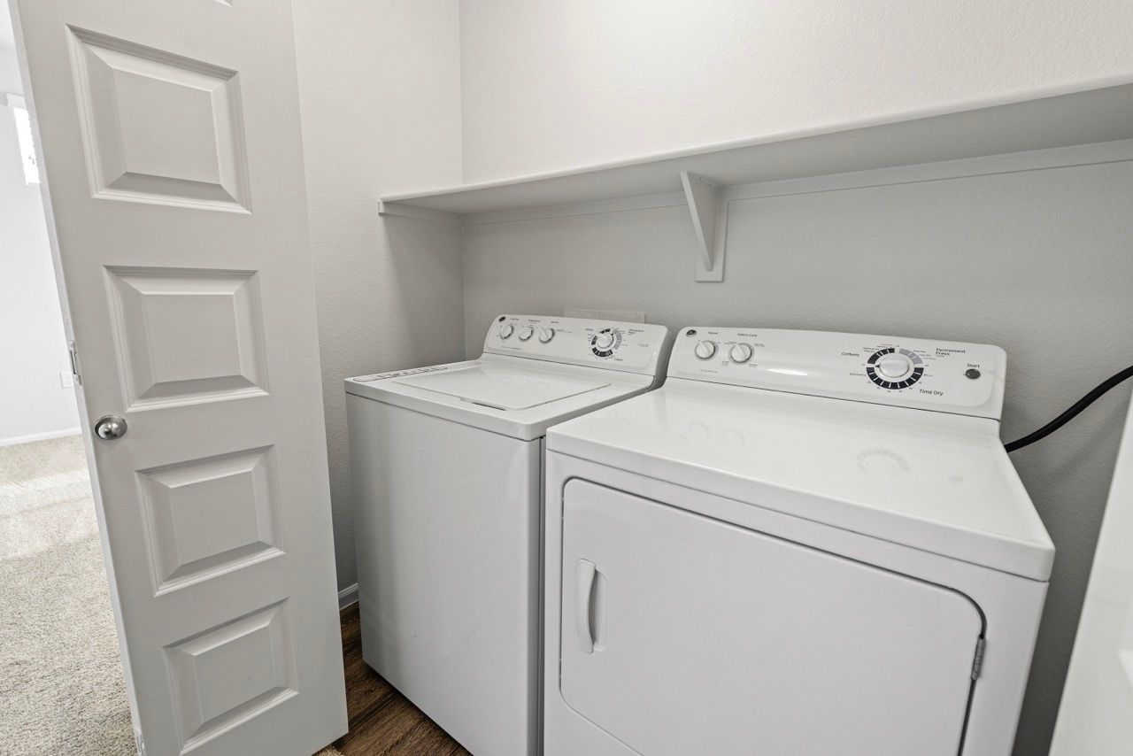 Laundry closet with a white washer and dryer side by side under a shelf.