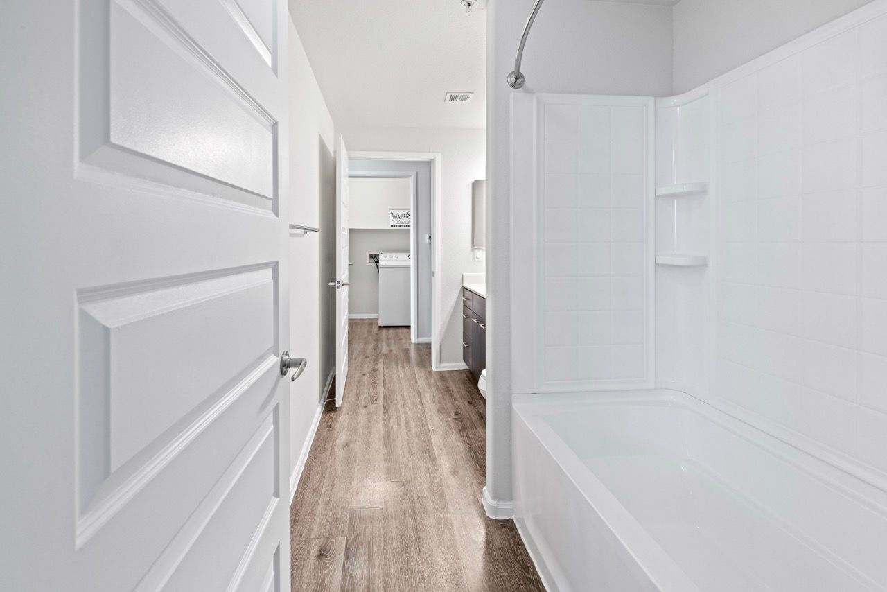 White bathroom with bathtub and shower; hallway leading to laundry area.