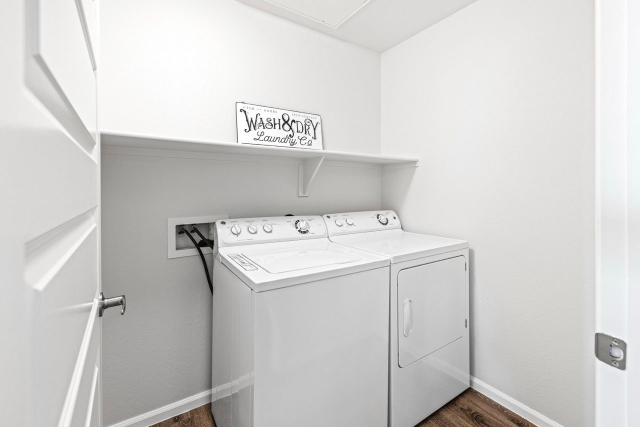 White washer and dryer side by side in a small laundry room with a shelf above.