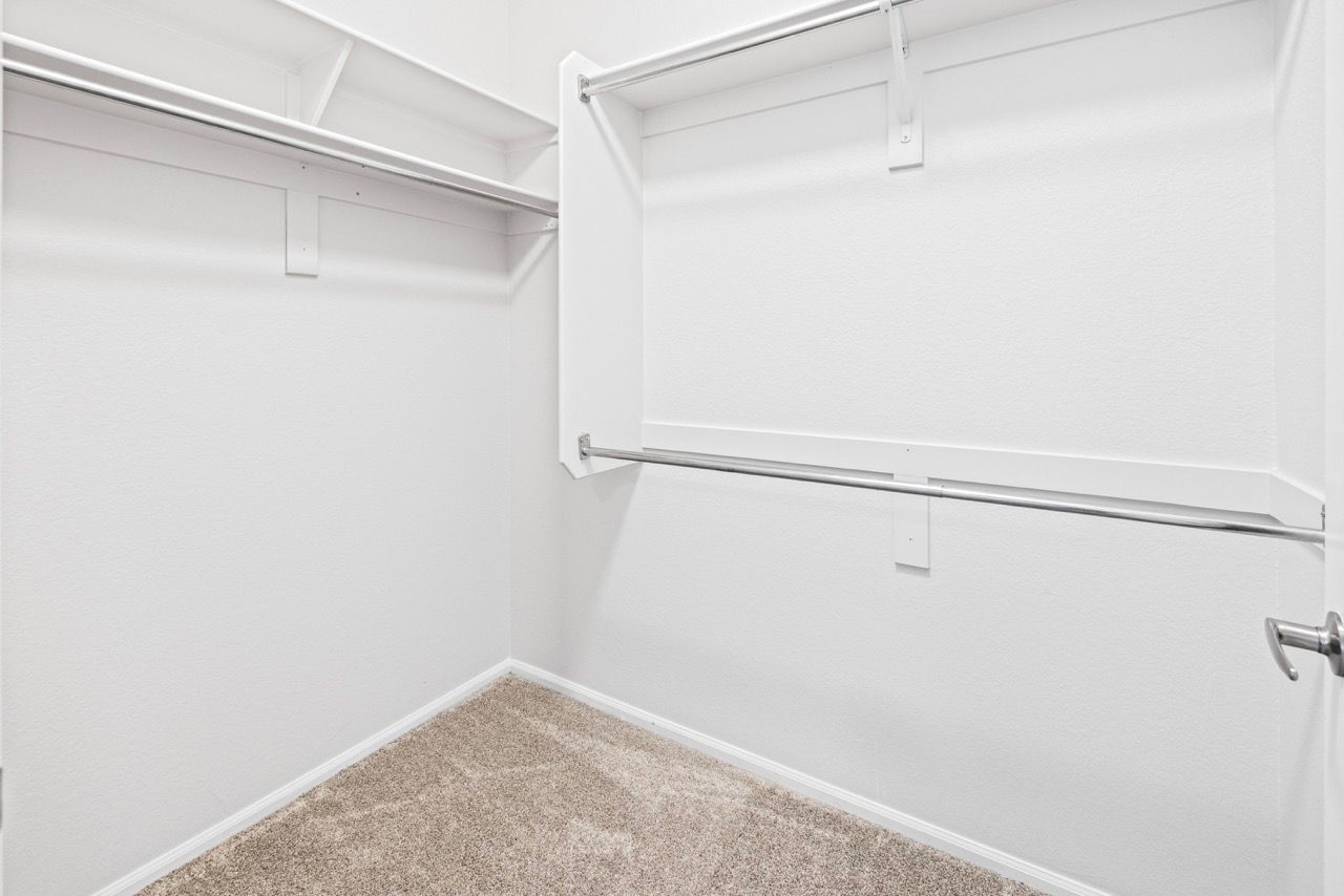 Walk-in closet with white walls, beige carpet, and metal double hanging rods.