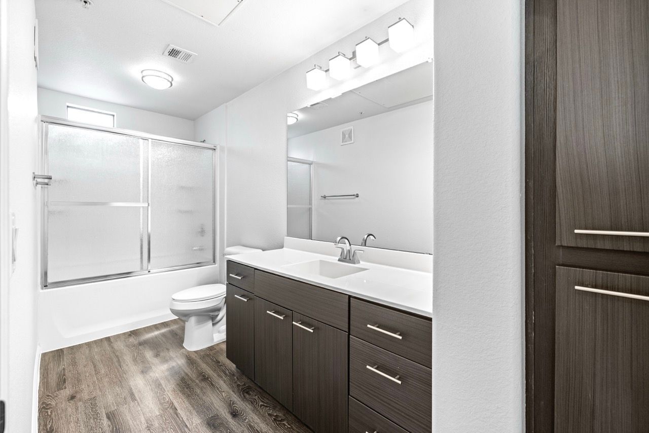 Bathroom with a dark wood vanity, white countertop, large mirror, and frosted glass tub/shower.