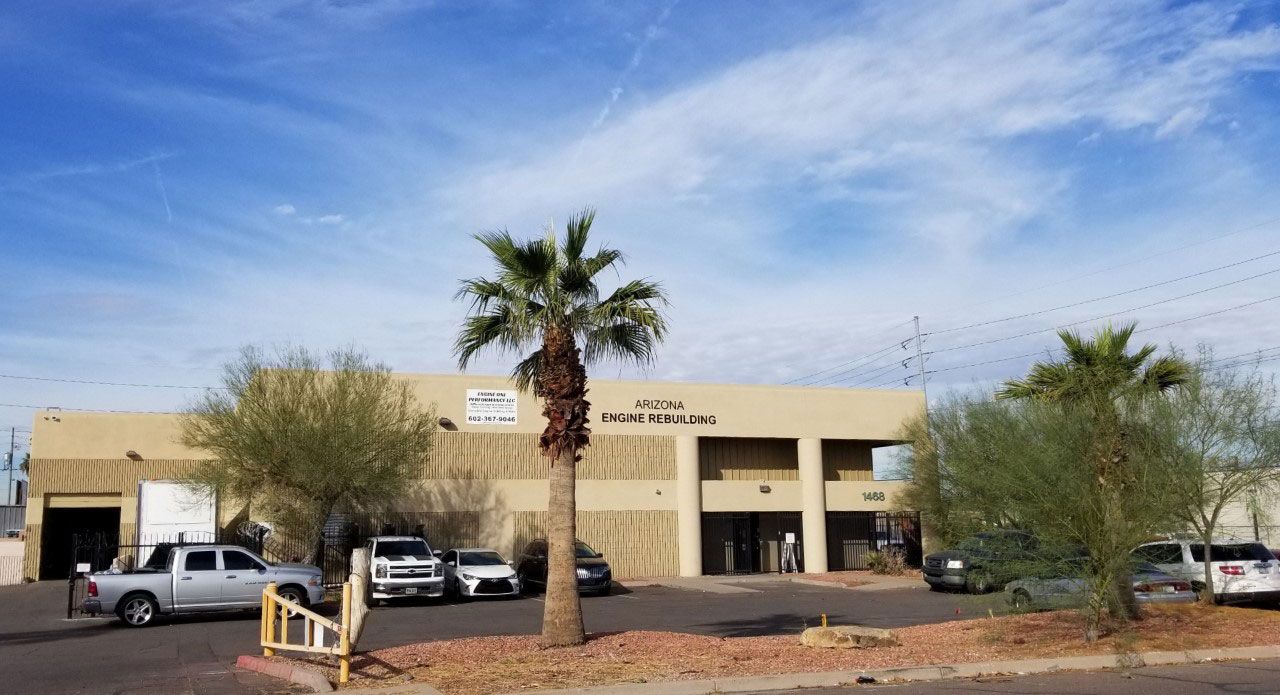 A light brown commercial building with a palm tree in front and parked vehicles; sunny, blue sky background. | Arizona Engine Rebuilding