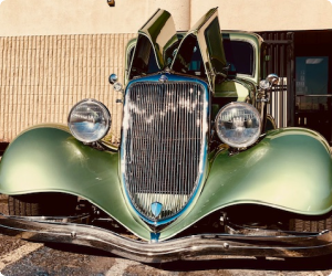 Green vintage car with open hood, parked in front of a building. | Arizona Engine Rebuilding