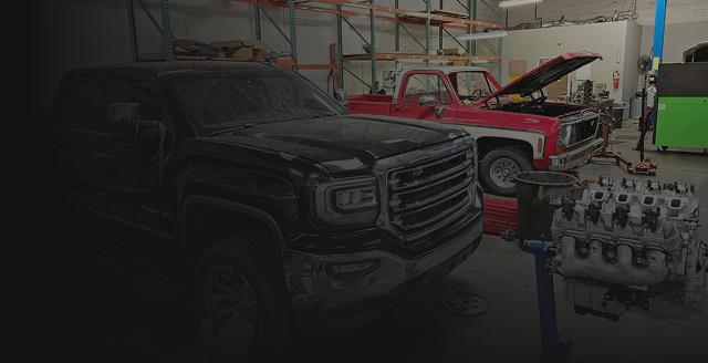Black truck in a garage next to a red truck with its hood open. Engine on stand in foreground. | Arizona Engine Rebuilding