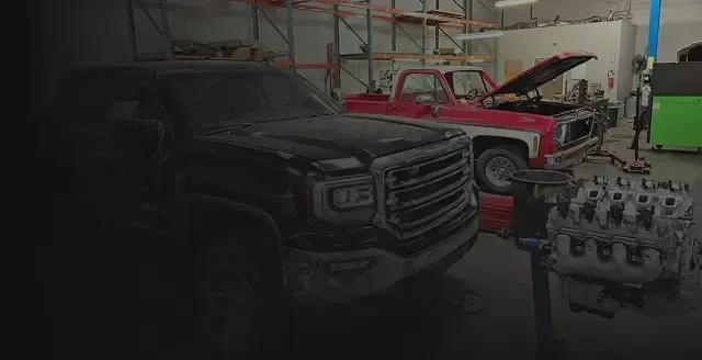 Black truck in a garage next to a red truck with its hood open. Engine on stand in foreground. | Arizona Engine Rebuilding