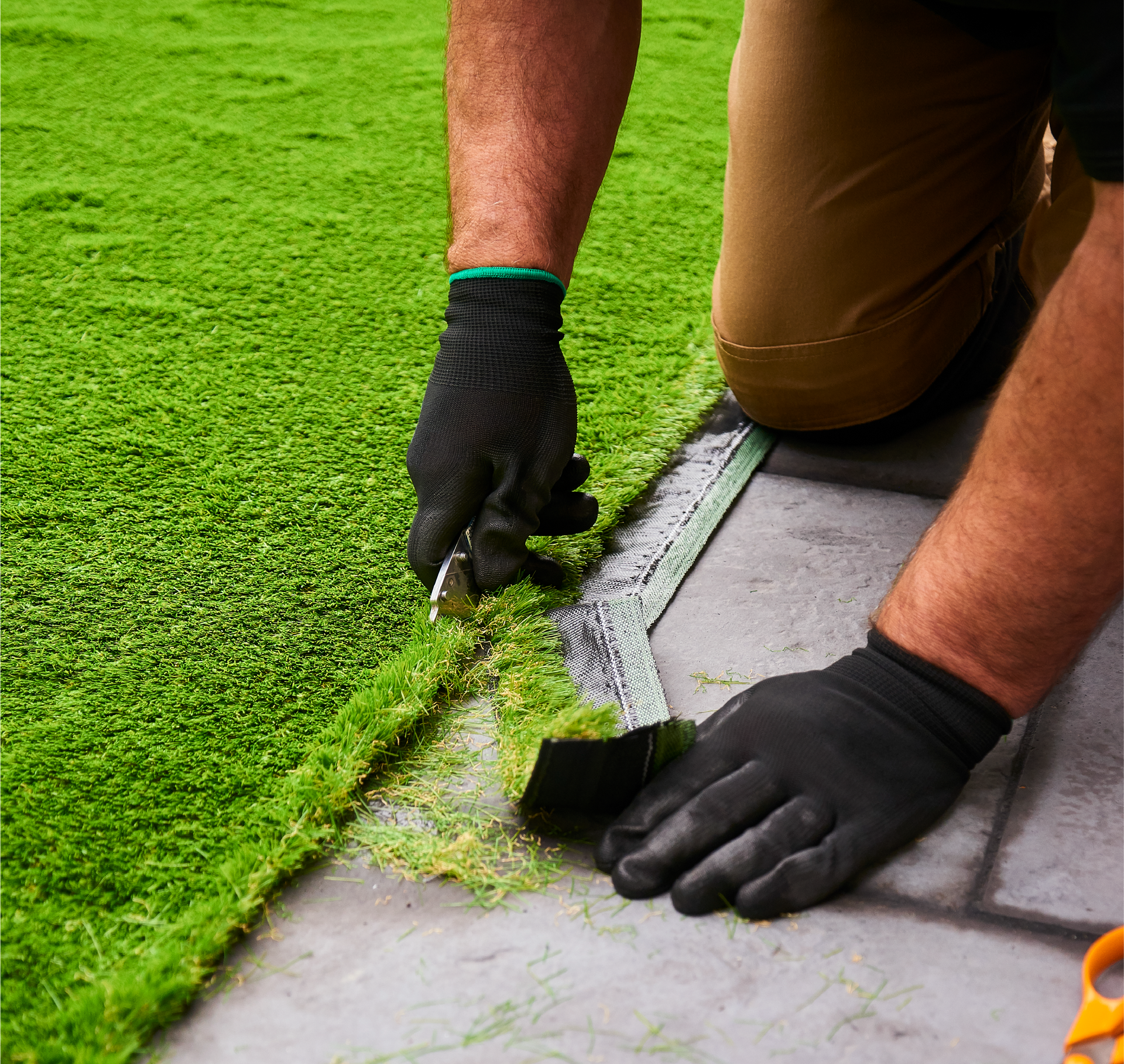 A man is cutting artificial grass with a pair of scissors.