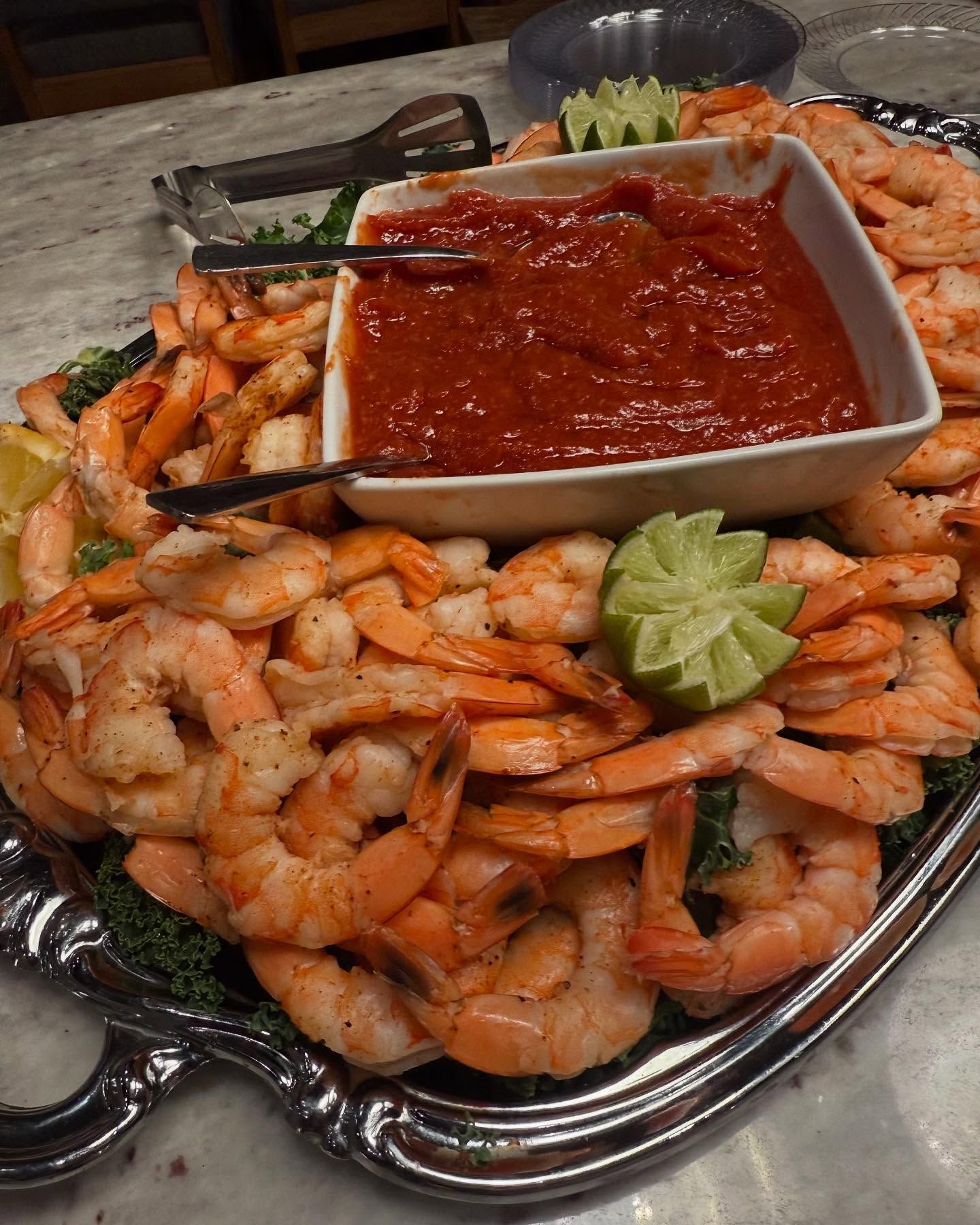 Tray of cooked shrimp with red cocktail sauce and lime wedges on a serving platter