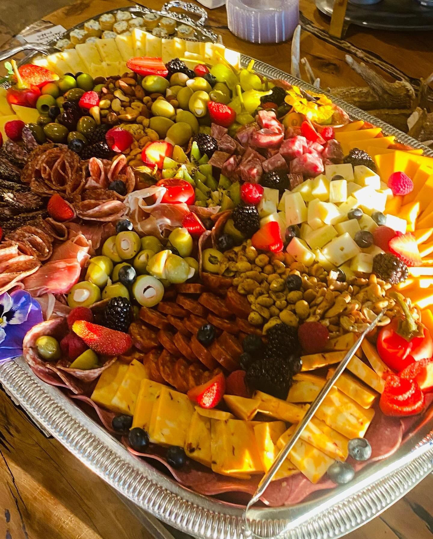 Assorted olives, cheeses, meats, and fruit arranged on a large silver serving tray