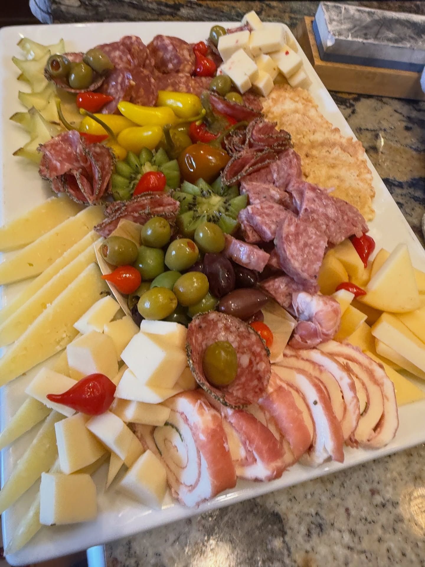 Assorted cheese, cured meats, olives, peppers, and crackers arranged on a charcuterie platter.