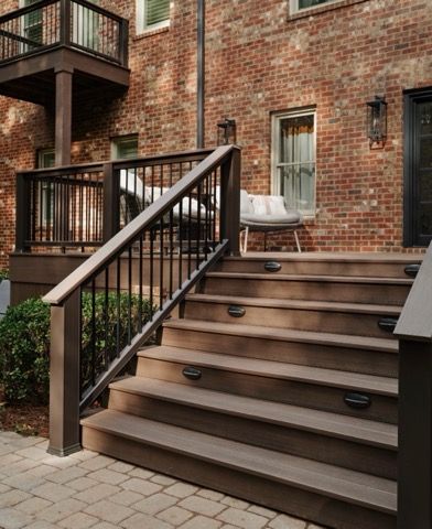 A wooden deck with stairs leading up to it and a brick building in the background.