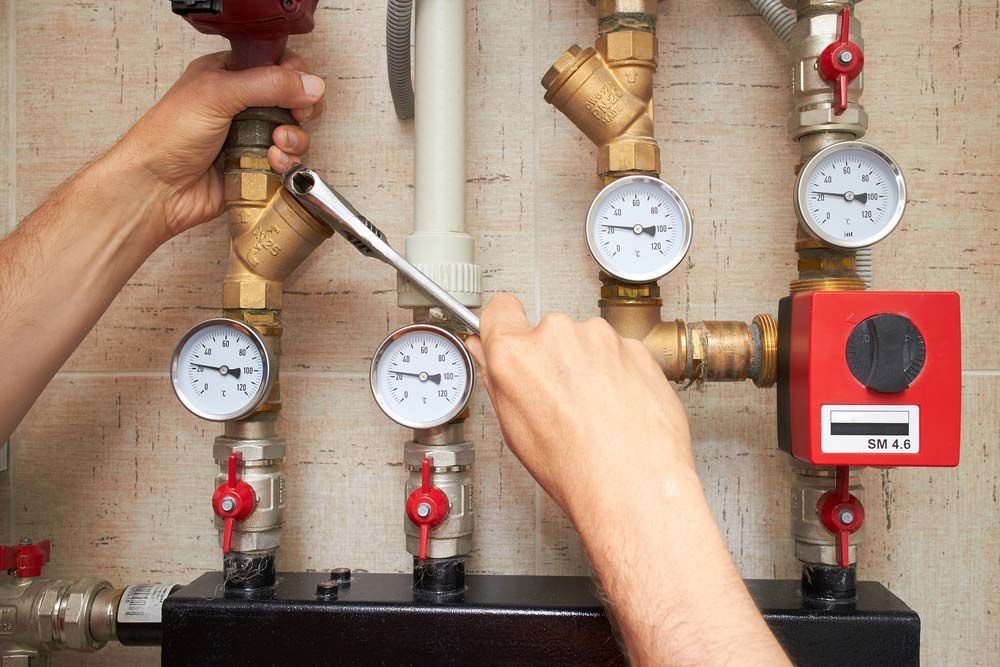 A Man is Working on a Heating System With a Wrench — Rock Plumbing & Gasfitting In Proserpine, QLD