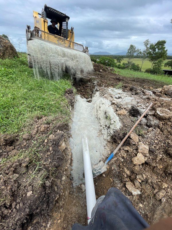 A Bulldozer Is Digging A Hole In The Ground Next To A Pipe — Rock Plumbing & Gasfitting In Cannonvale, QLD