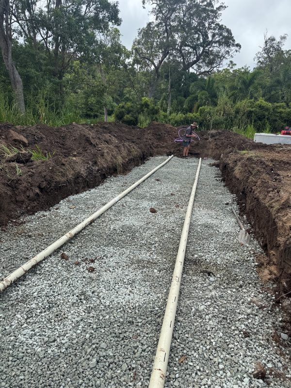 A Man Is Digging A Trench In The Dirt With Pipes In It — Rock Plumbing & Gasfitting In Cannonvale, QLD