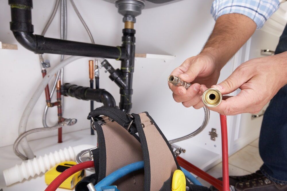 A Plumber is Fixing a Pipe Under a Sink — Rock Plumbing & Gasfitting In Cannonvale, QLD