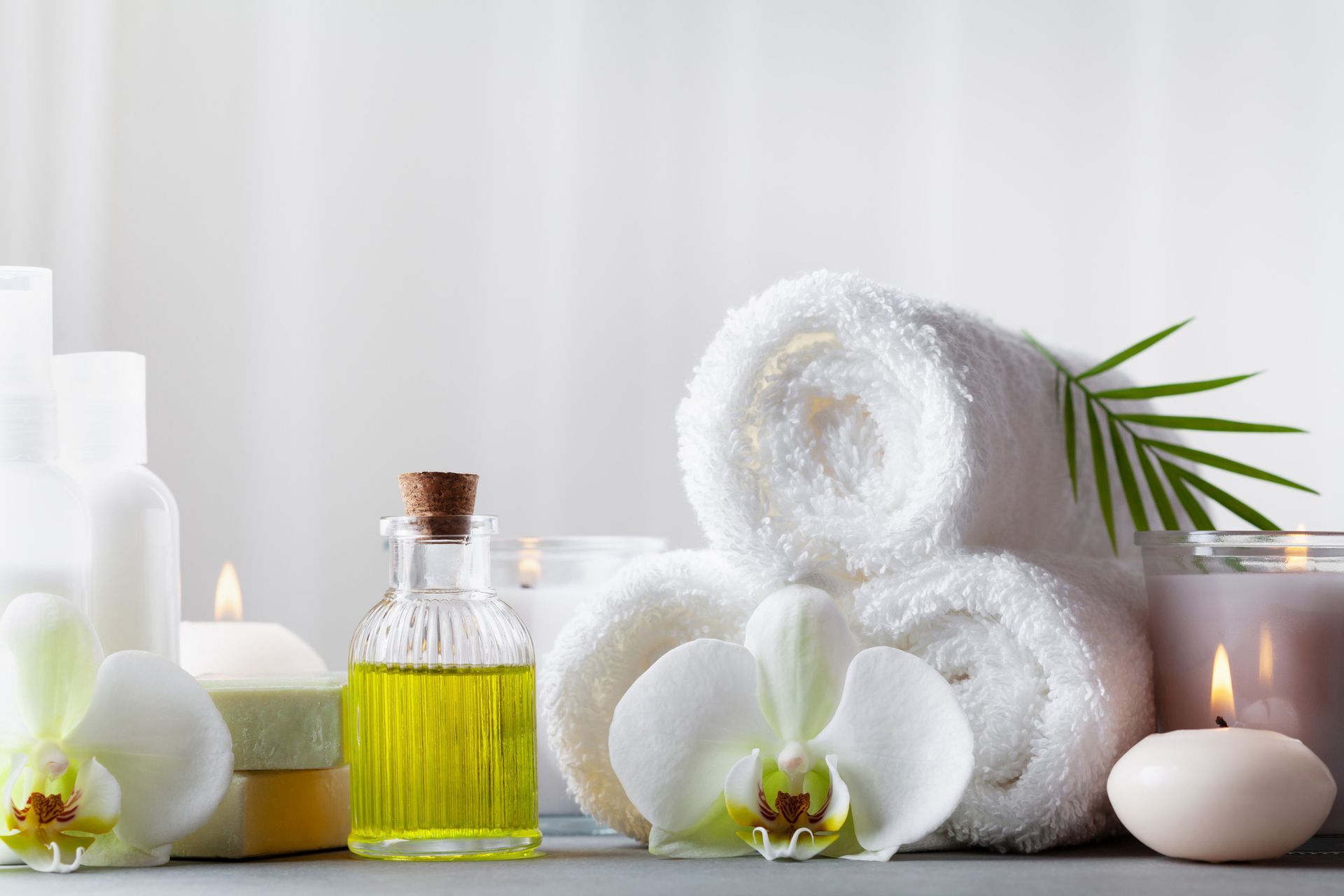 A table topped with towels , candles , soap , oil and flowers.