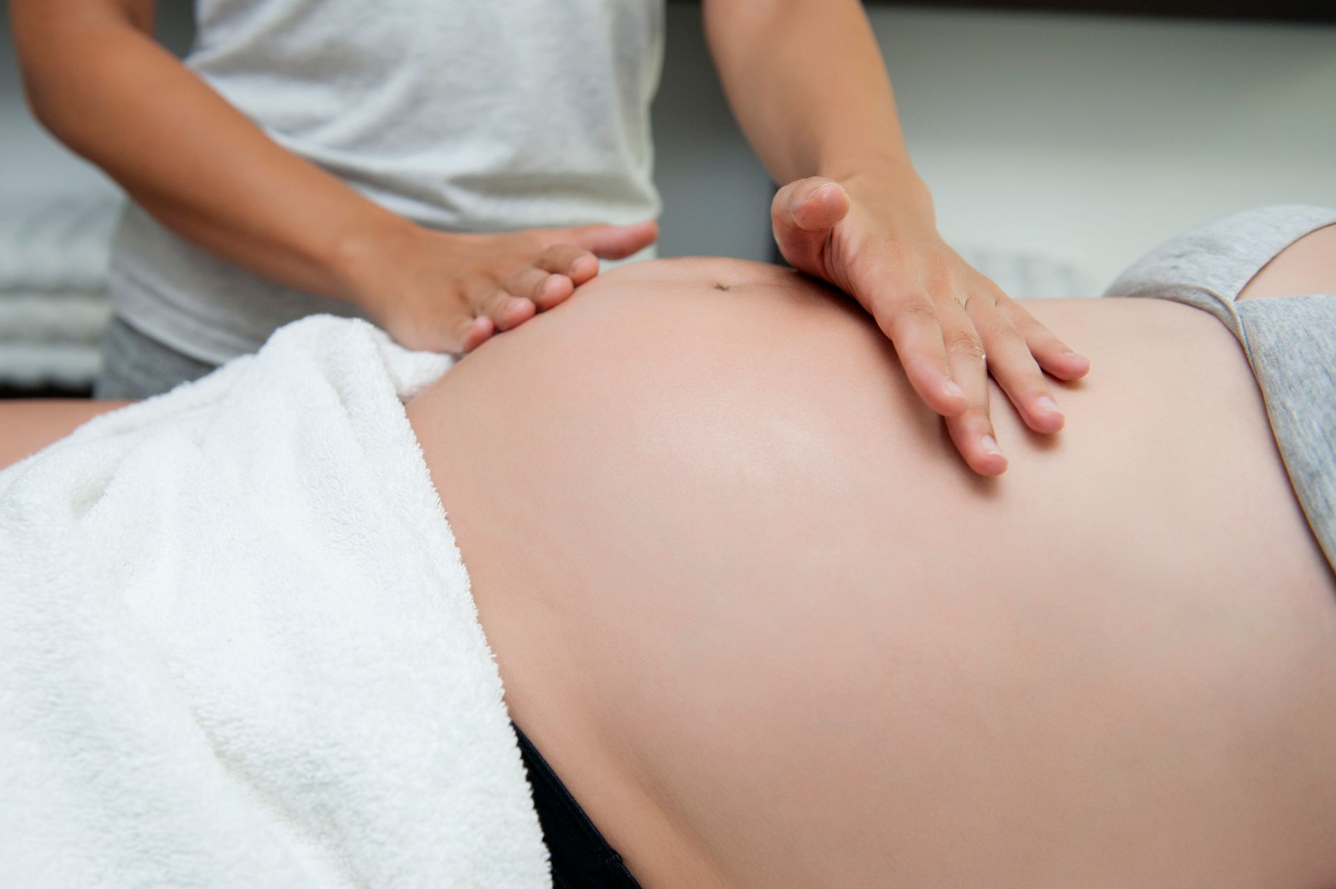 Female massage therapist's hands massaging a pregnant woman's stomach.