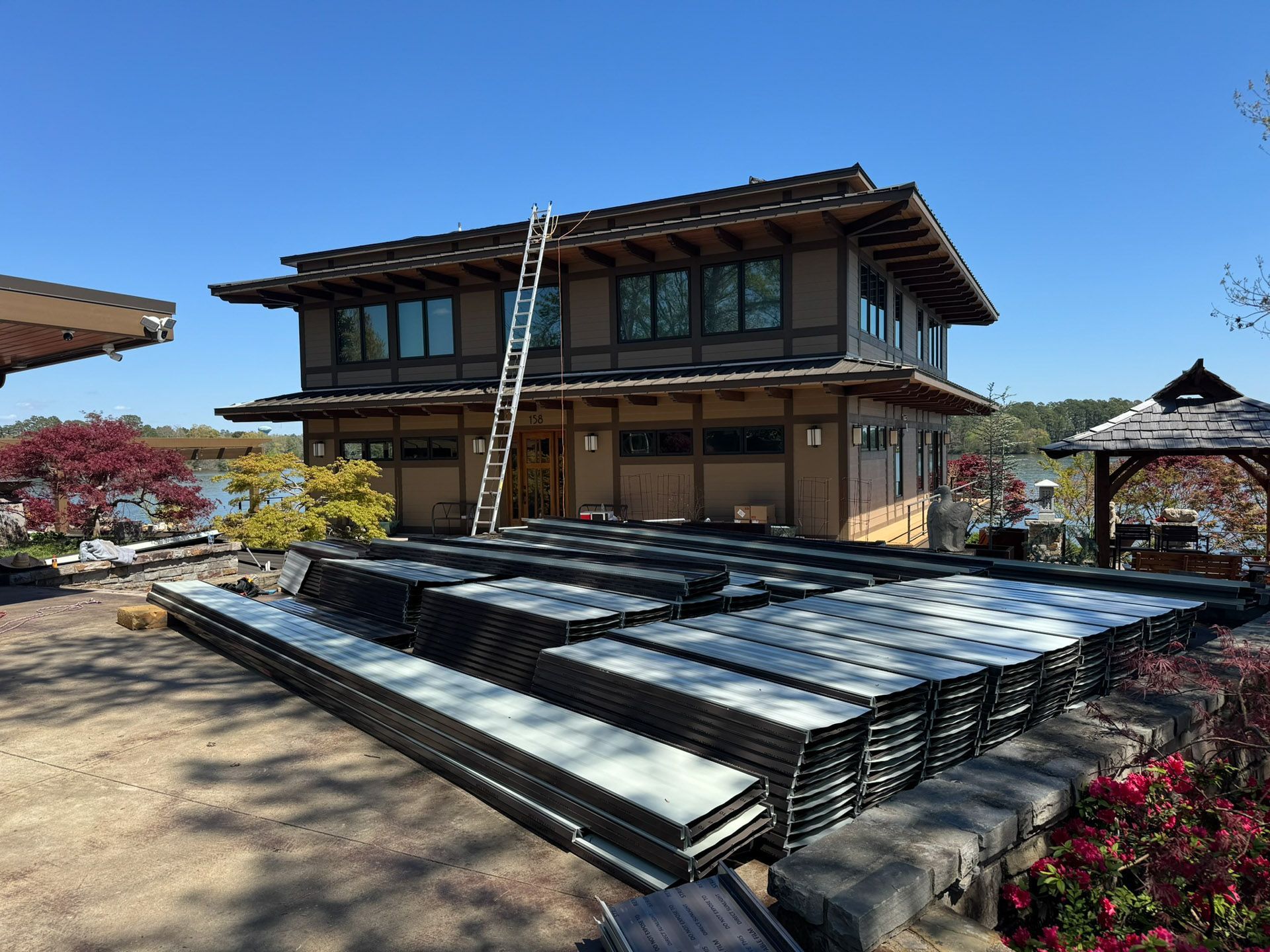 A wooden house under construction with stacked metal beams and a ladder against the facade under a blue sky.
