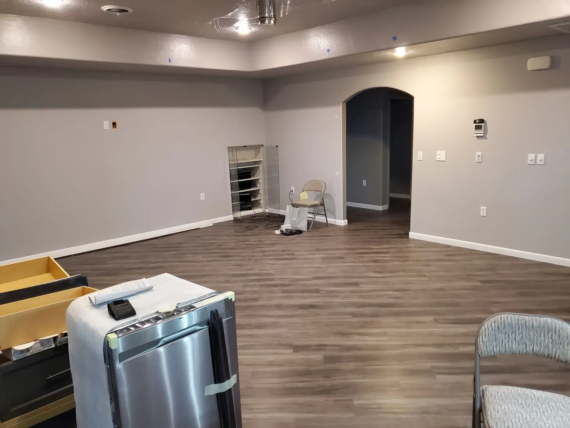 Empty gray room with wood-look flooring, arched doorway, and a few cleaning supplies near the wall