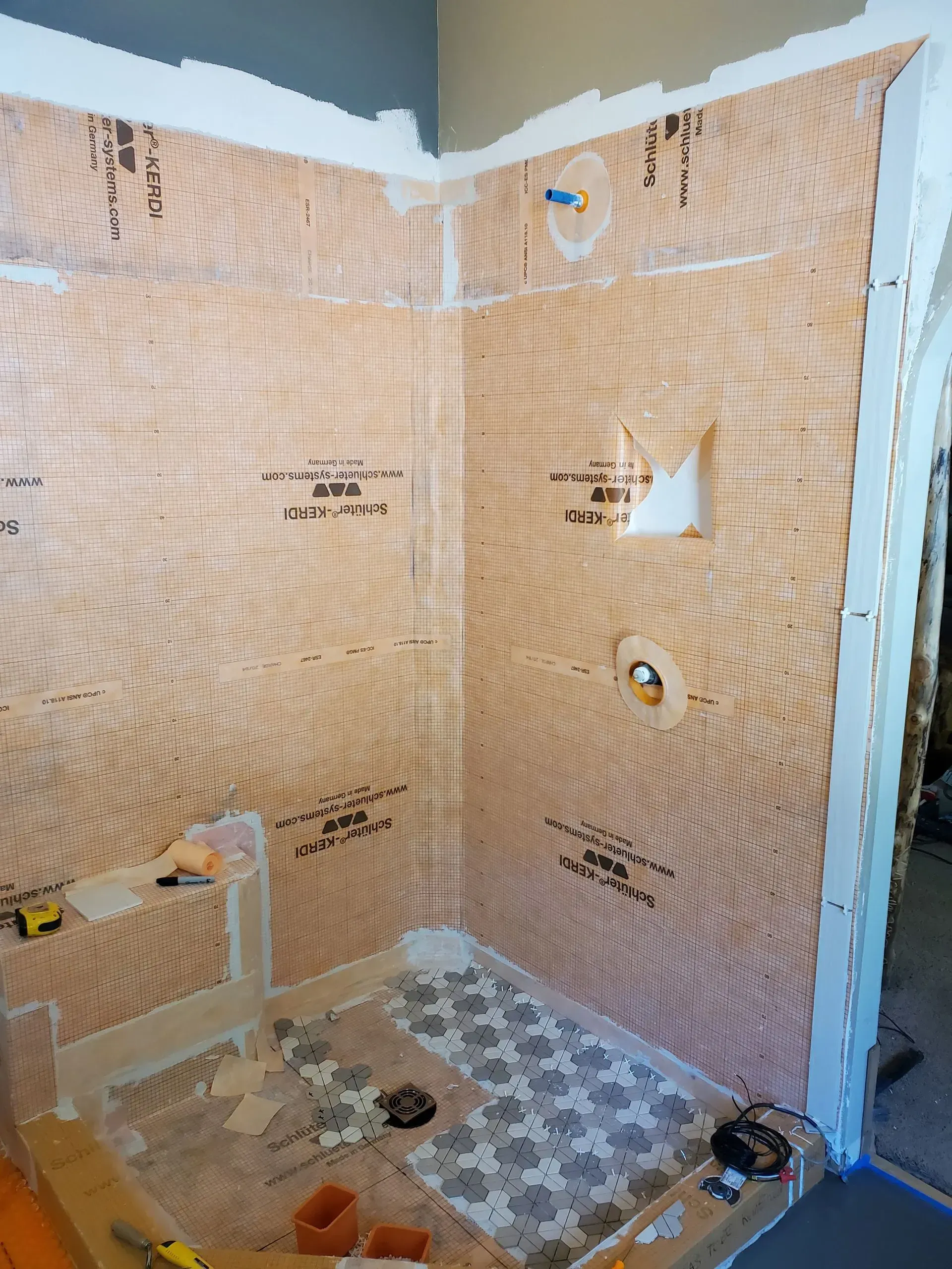 Bathroom under renovation with exposed wall insulation, tiled shower floor, and construction materials.