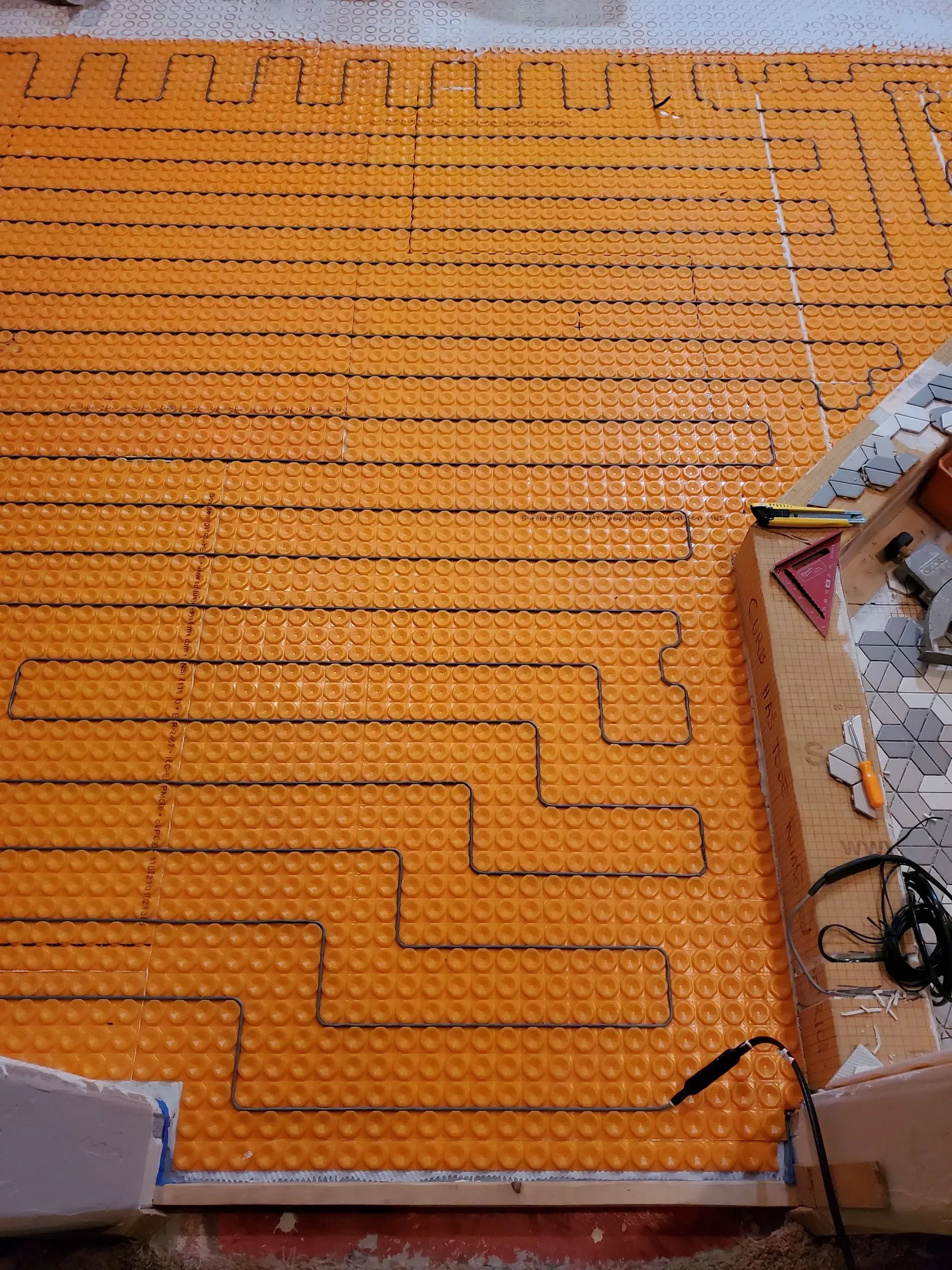 Orange heated floor with black tubing laid in a serpentine pattern, likely underfloor heating installation