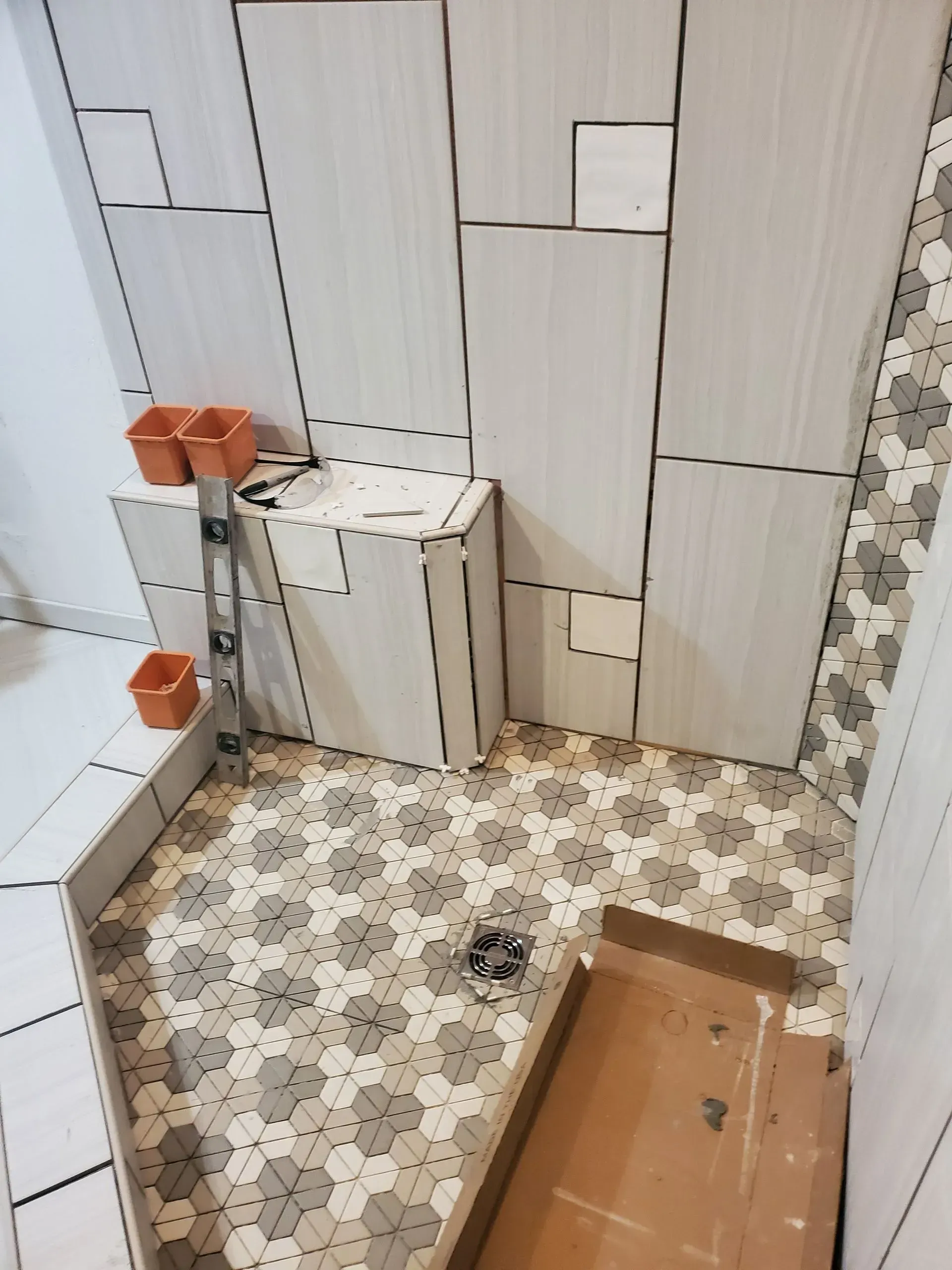 Small tiled bathroom with patterned floor, white wall tiles, and a wooden box on the floor.
